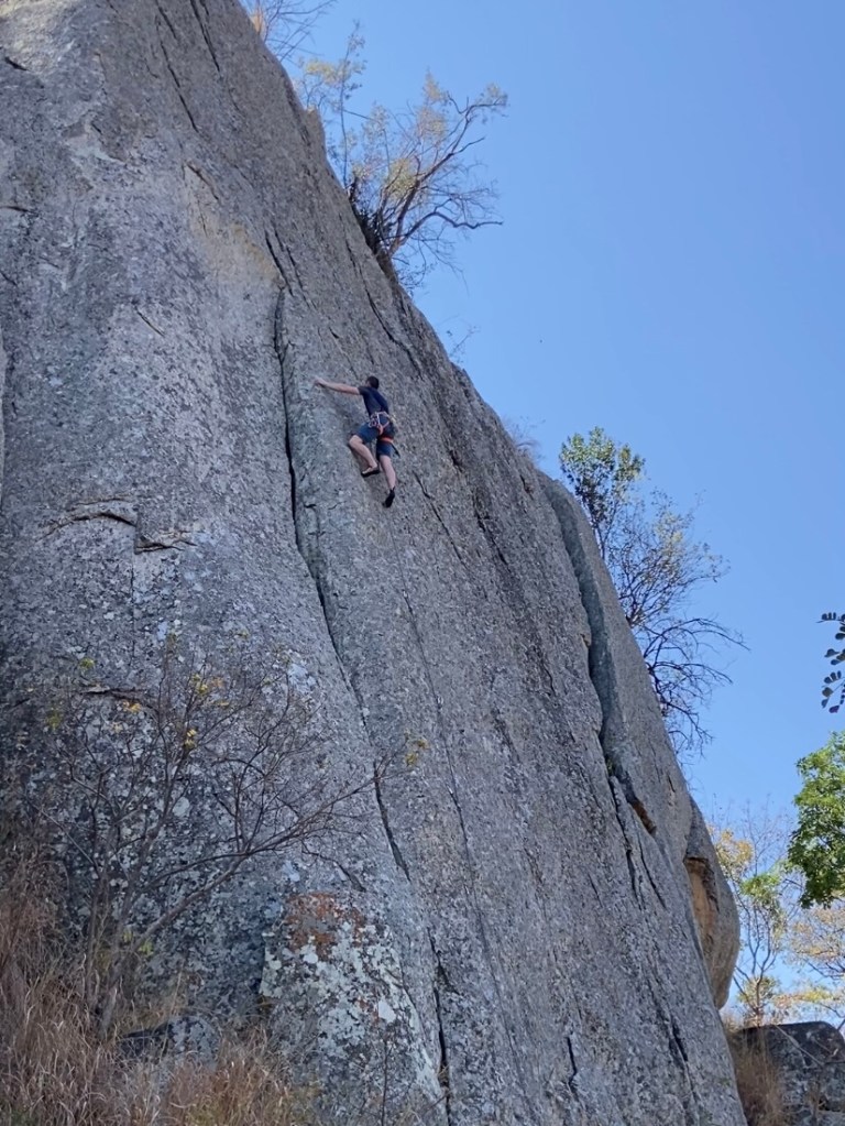 Climber on grey slabby wall with flake and crack features. 