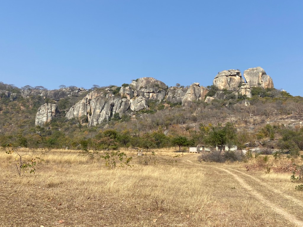 Granite pinnacles on the hill top. At the base of the hill is a small holding among the trees and bush. 