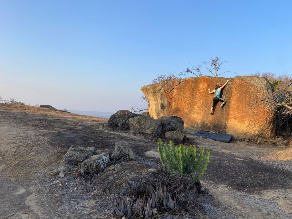 Climber traversing along a seam on a orange granite boulder on top of a grey granite plateau. 