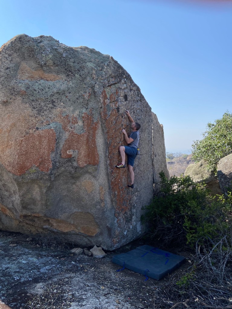 Climber on vertical wall on the side of a large granite boulder.
