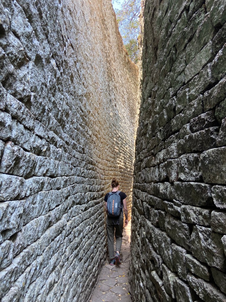 Person walking in a passageway between two tall stone walls. 