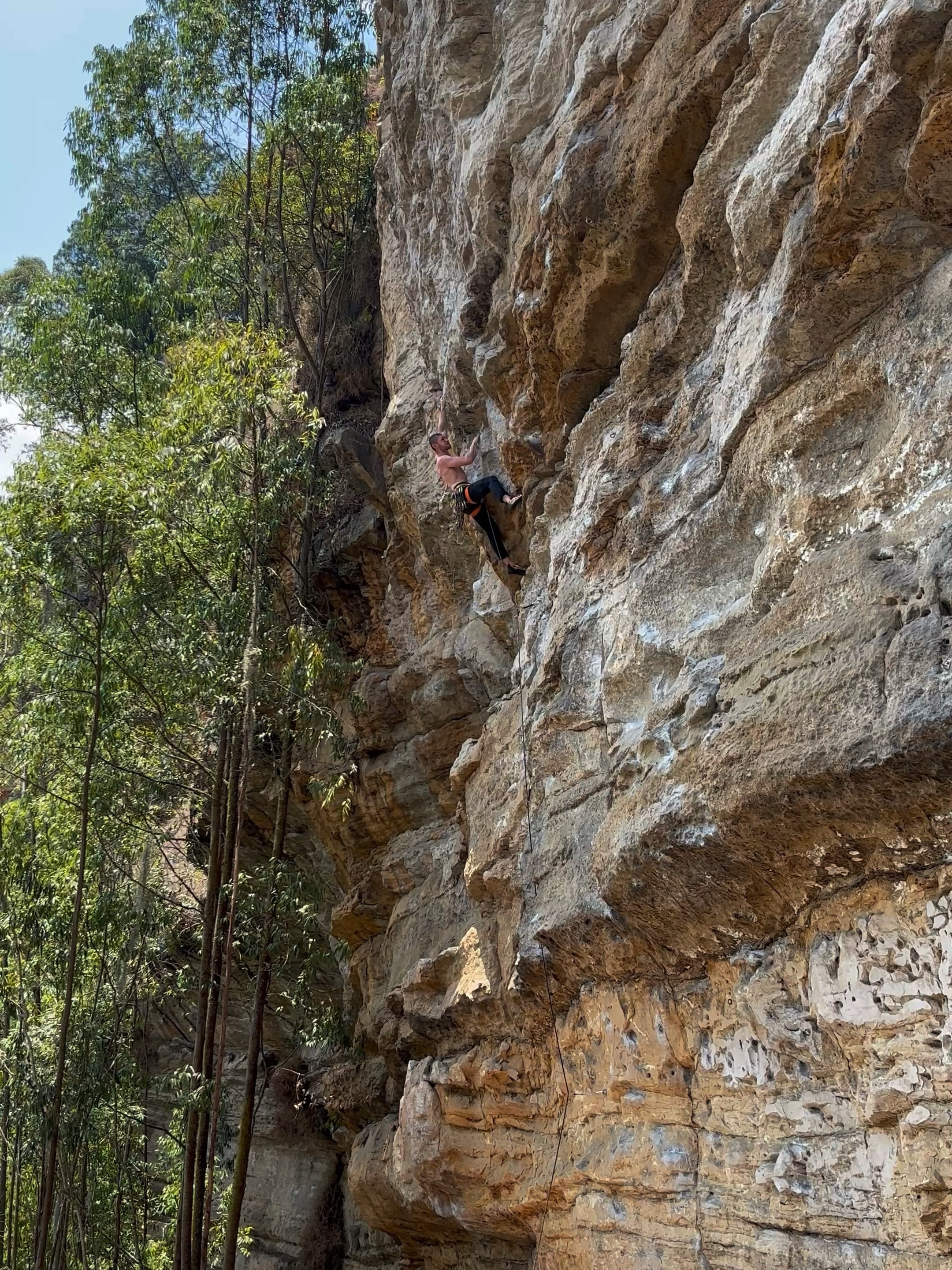 Climber on a steep yellow orange sandstone wall pulling through the crux moves on an overlap. 