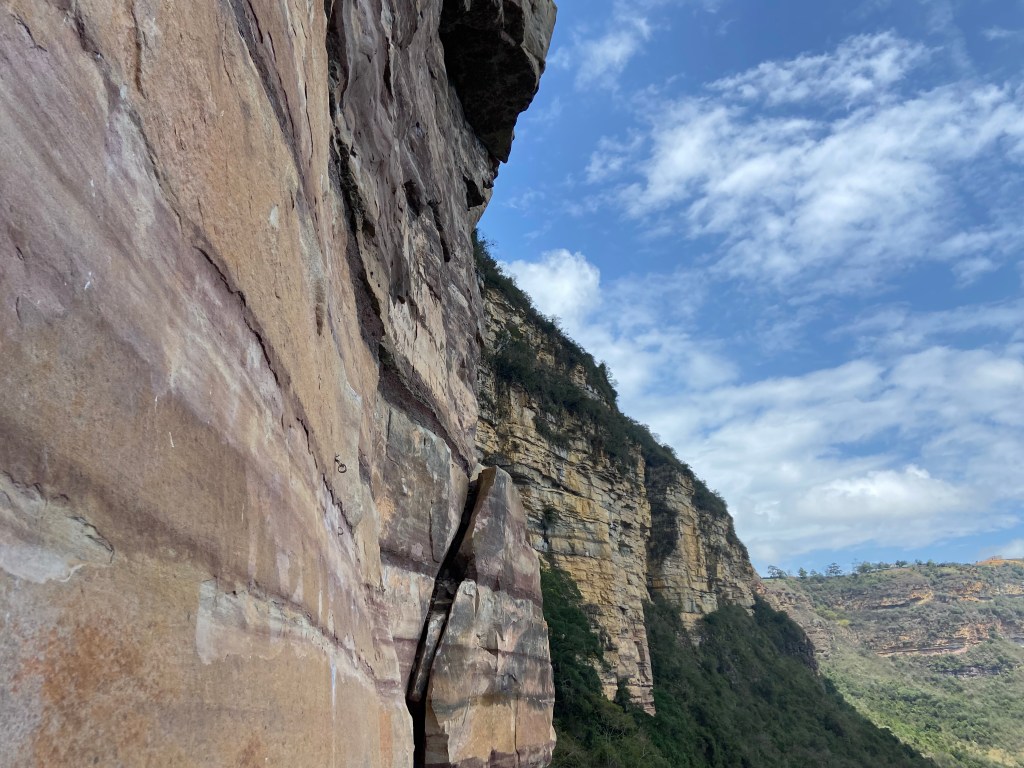Band of yellow and grey sandstone rock set upon the lush green hillside. 