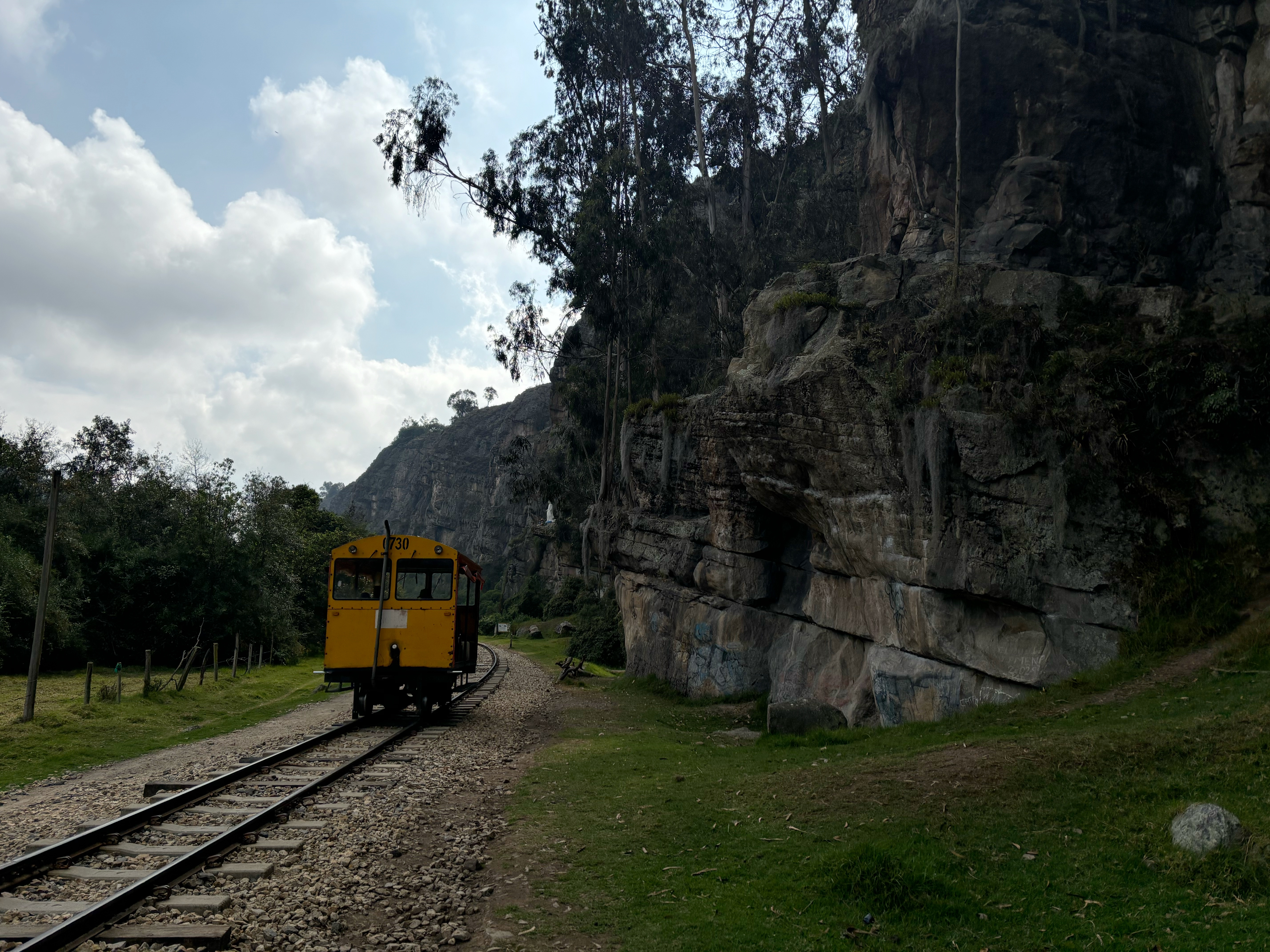 Yellow train cart on tracks that run by the base of a sandstone crag.