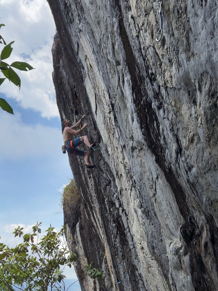Climber looking for the next hand move on a steep granite crag with black and white stripes. 