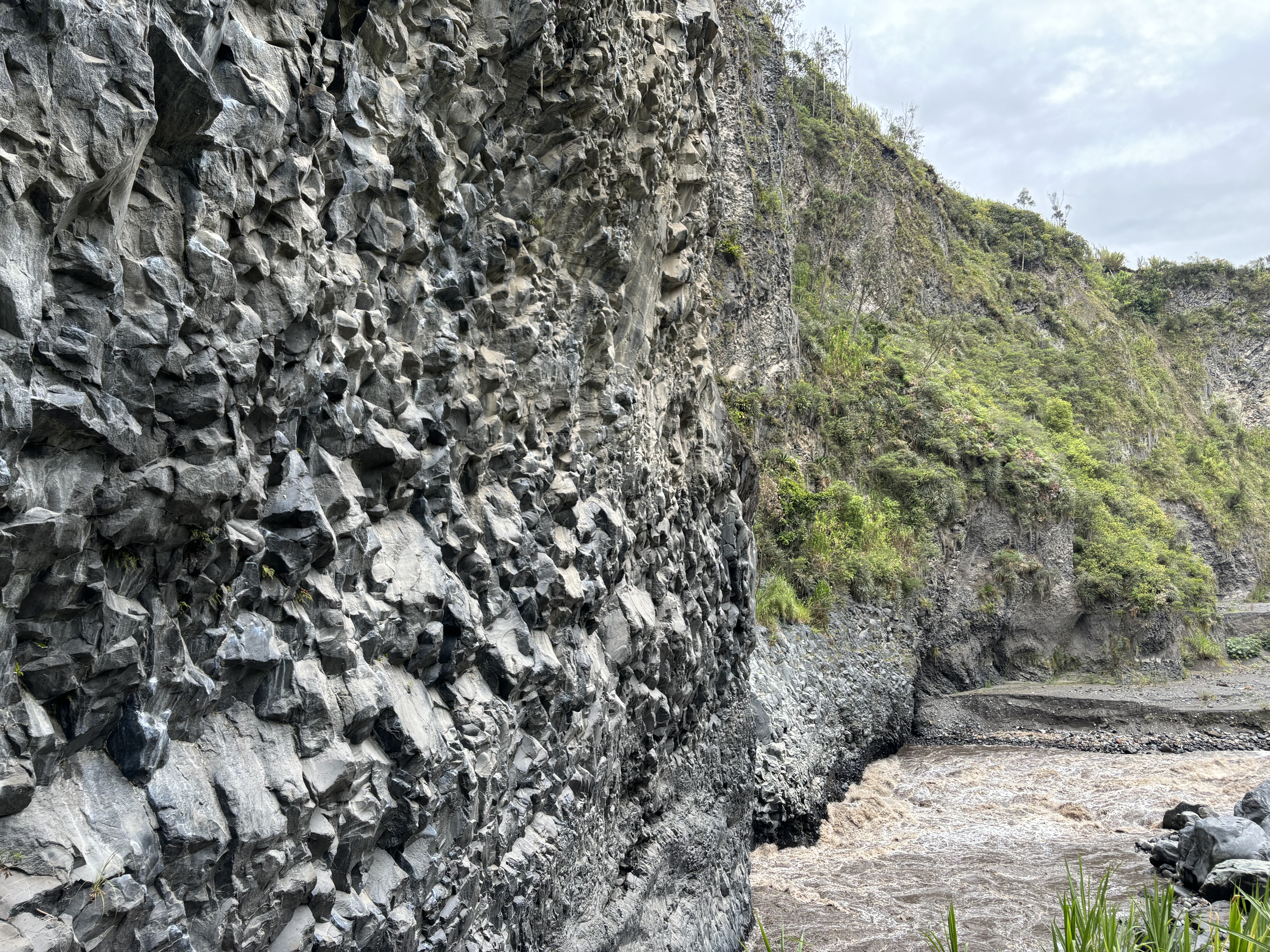 Heavily featured dark basalt wall above a fast flowing river. 