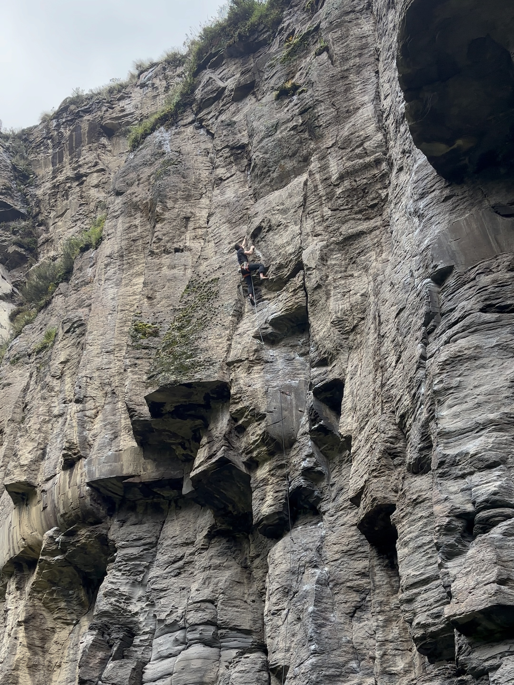 Climber pulling through steep section of dark wall of volcanic rock.