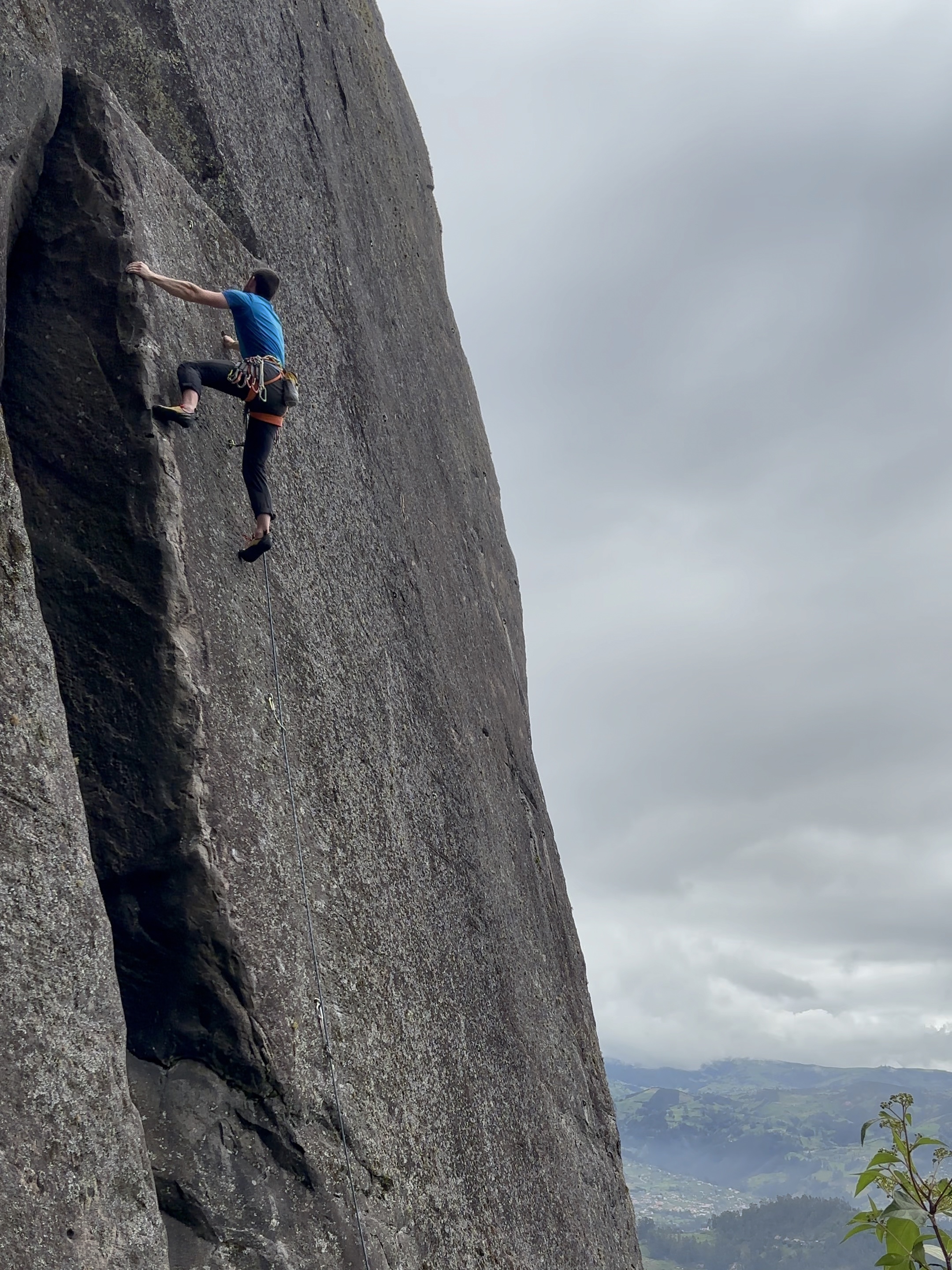 Climber on blank grey slab using an arête for the left hand and foot to make their way upwards.