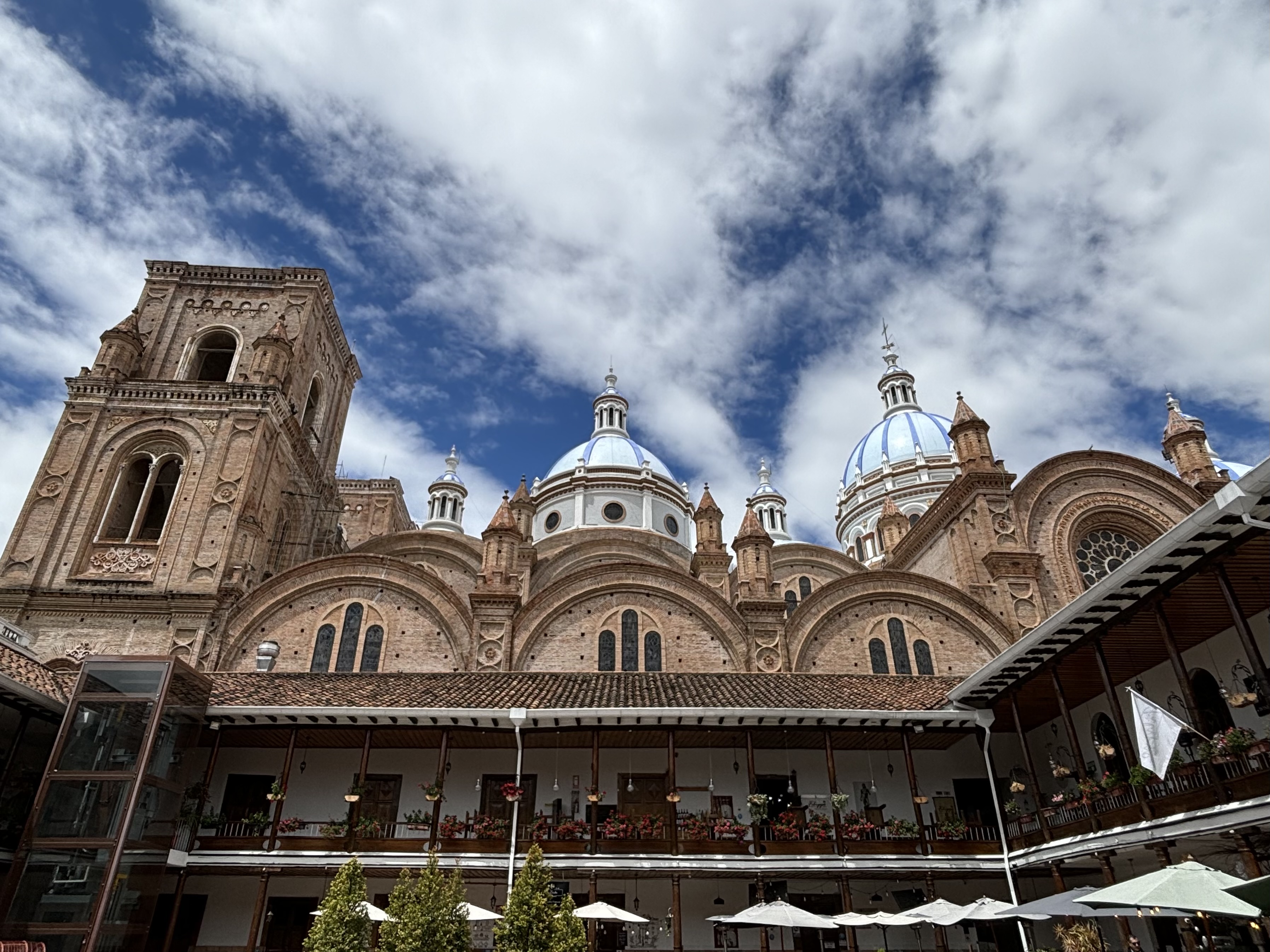 Large and imposing brick church with multiple archways with white and blue domes behind a serene courtyard. 