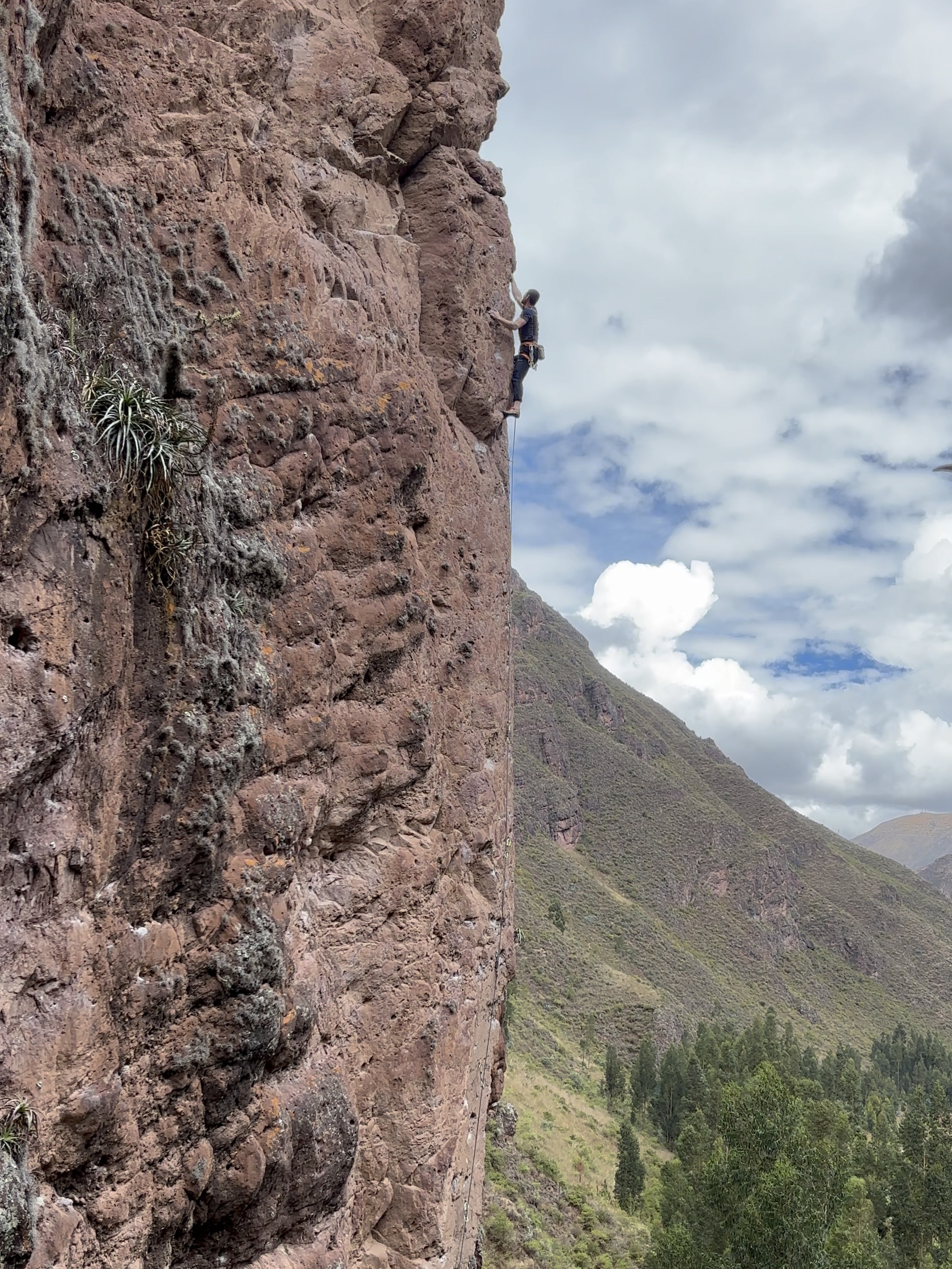 Climber on an arête of orange/pink coloured rock above a forest. 