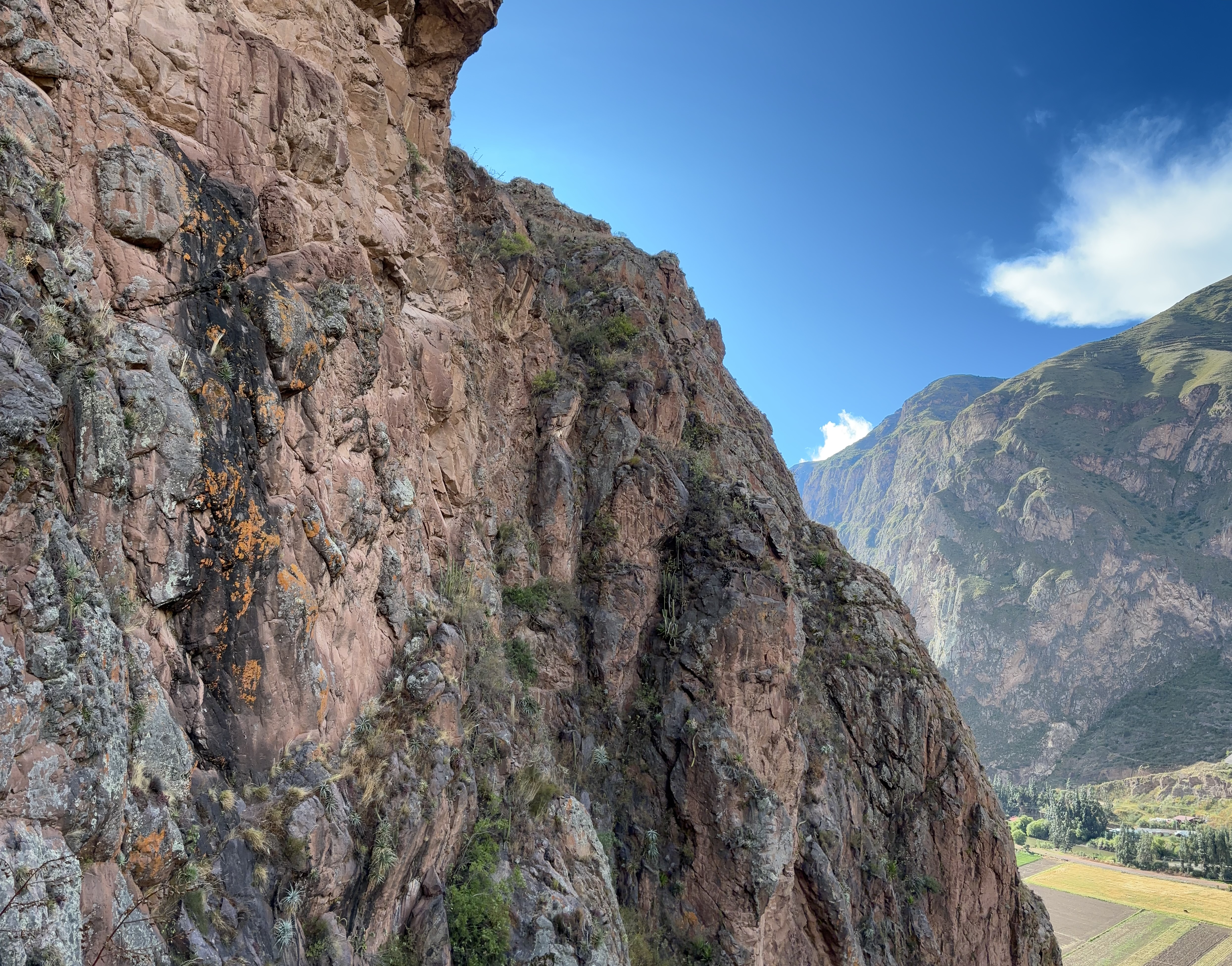 Black streak on an orange pink wall set on a steep sided hill with fields below. 