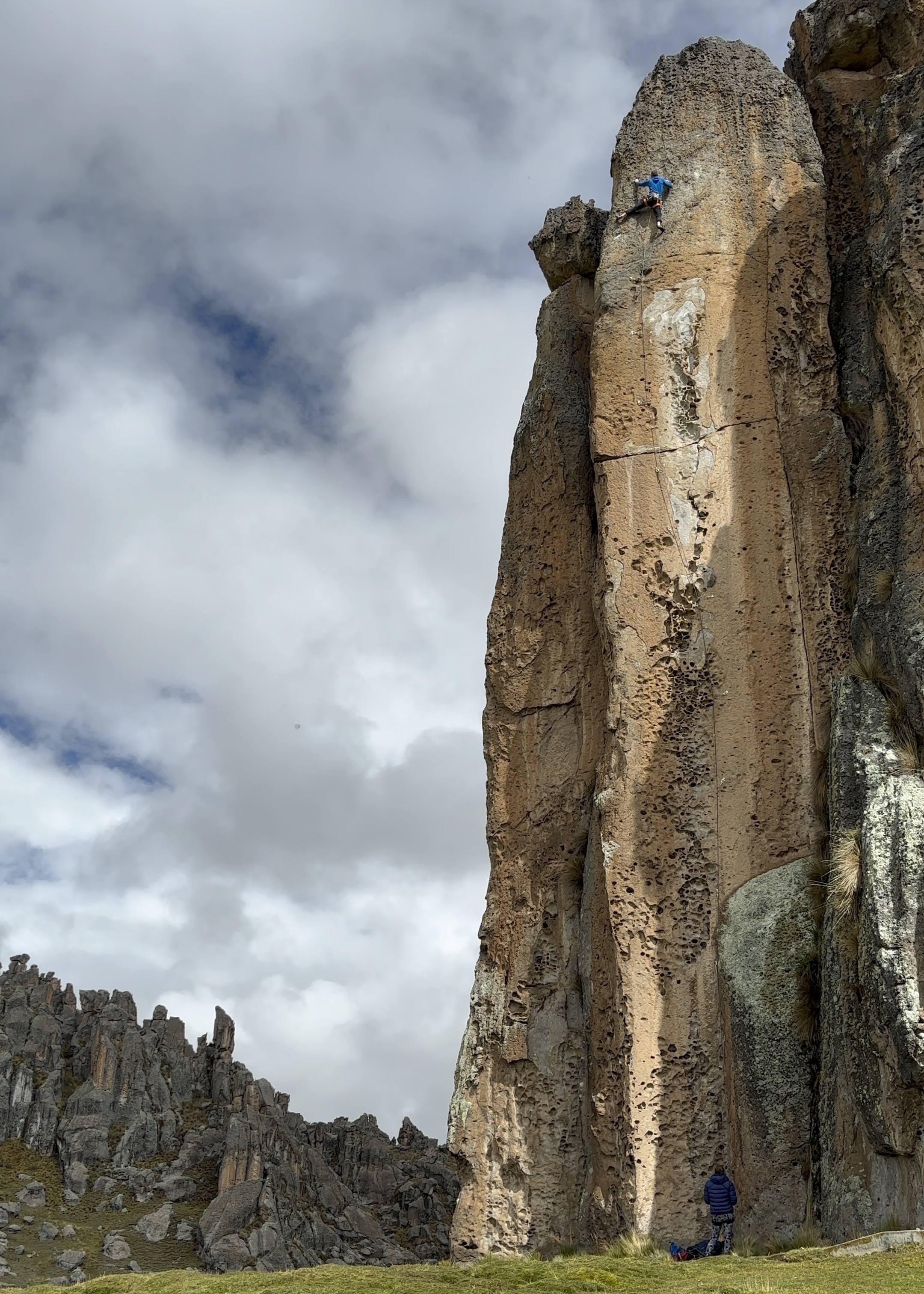 Climber balancing up a pillar like feature on a vertical rock face, in the background are many other rock pillars which form a forest of stones. 