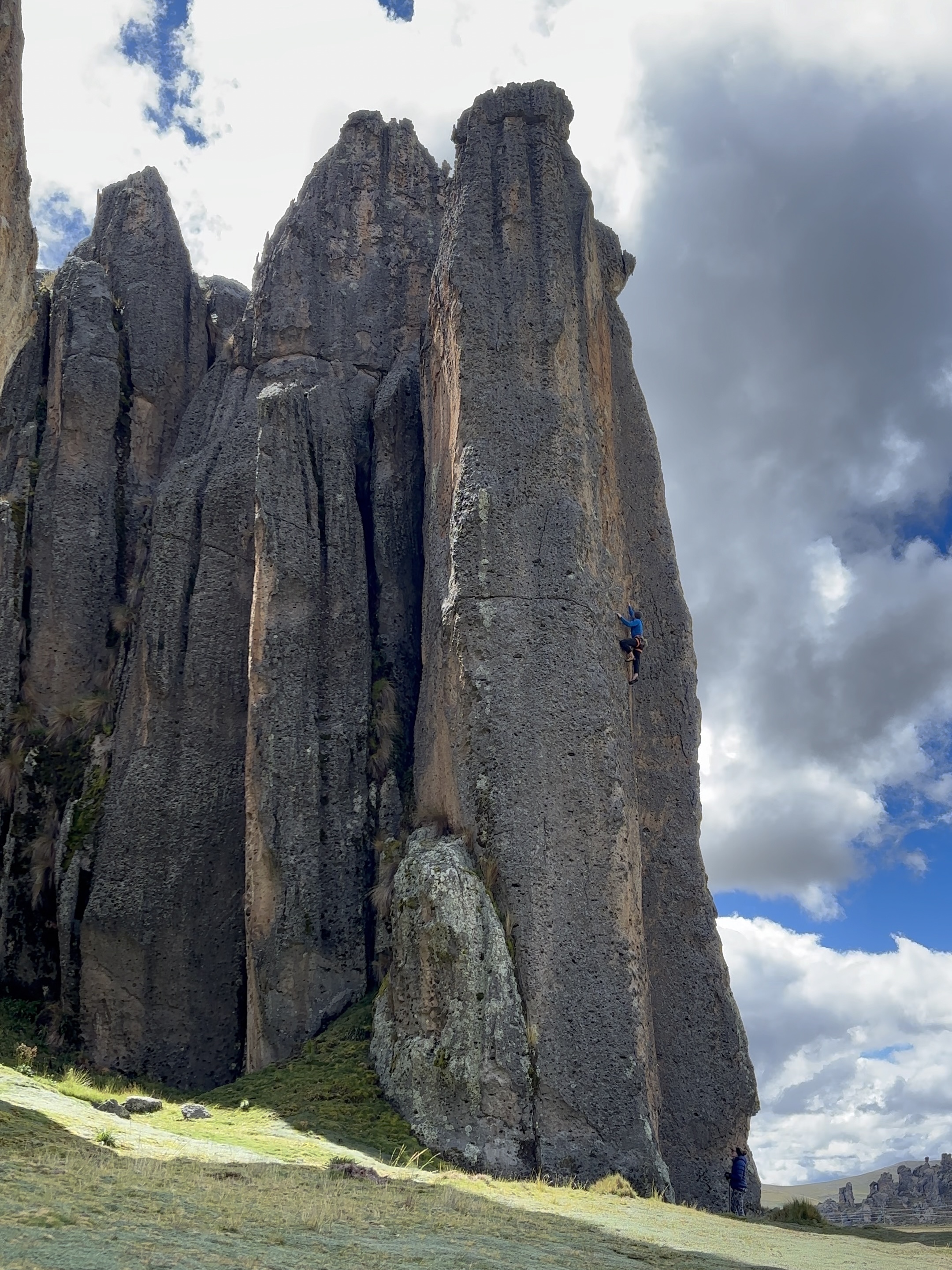 Climber in a blue fleece on a volcanic rock pillar set within a stone forest rock formation. 