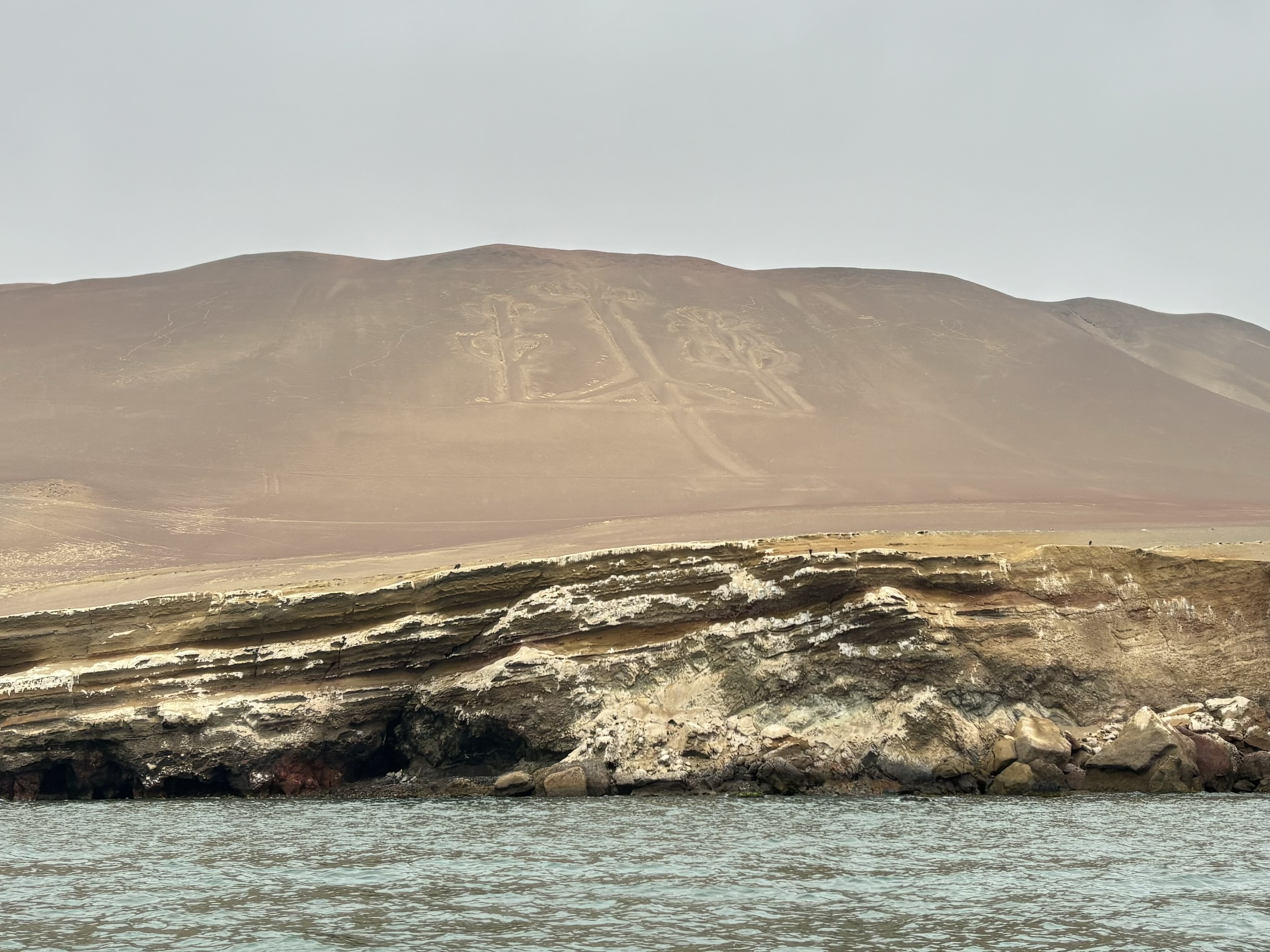 The outline of a candelabra drawn into the sand set upon a sandy hillside on the coastline. 