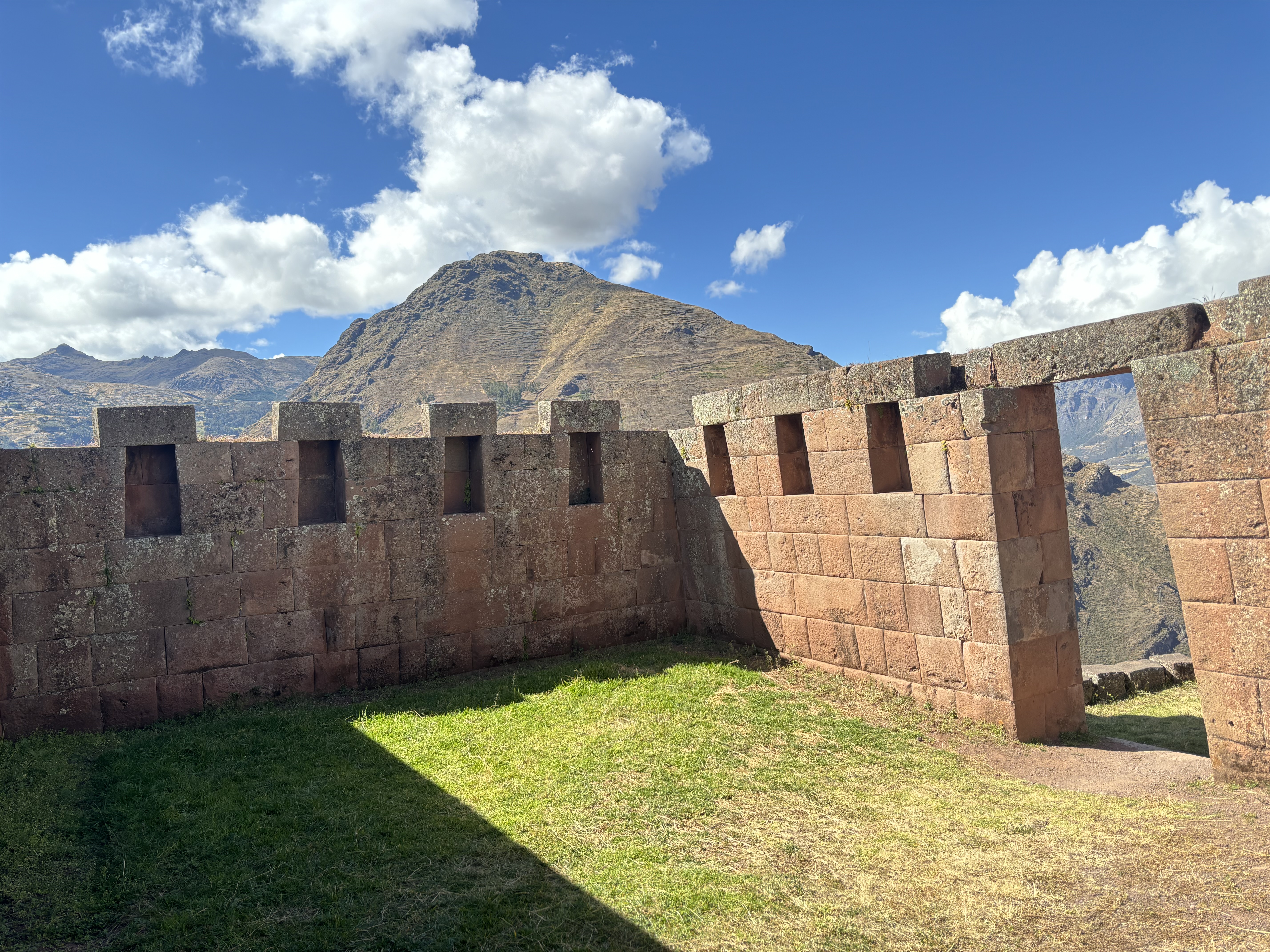 Incan ruin with a doorway and  seven alcoves set within the stone walls. Surrounding the ruins are steep, high altitude mountains.