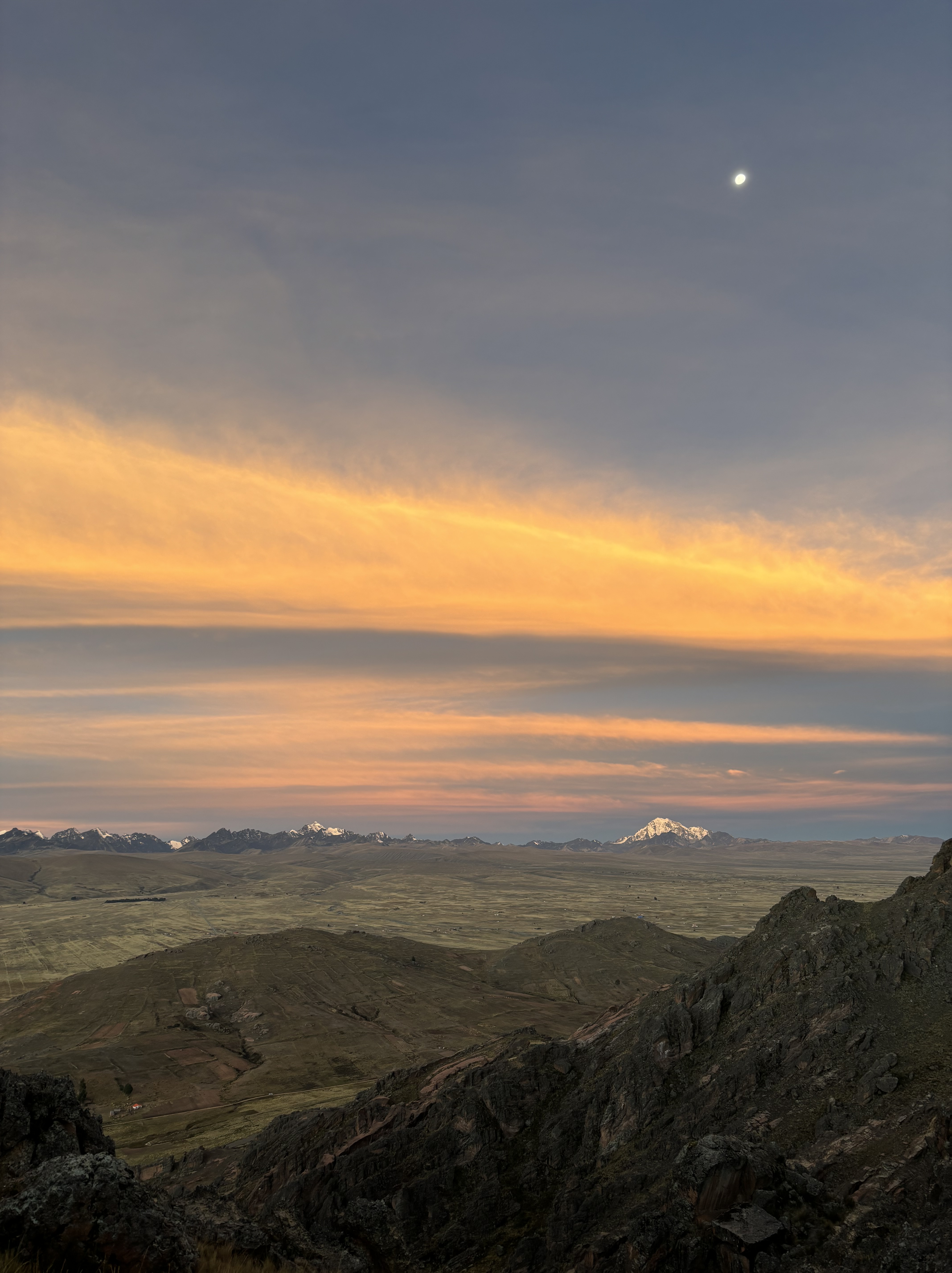 Snow capped, high altitude mountains in the distance at sunset.