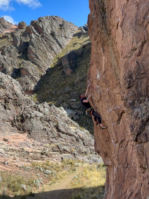 Climber pulling hard on overhanging orange sandstone with grey fins of rock in the background.