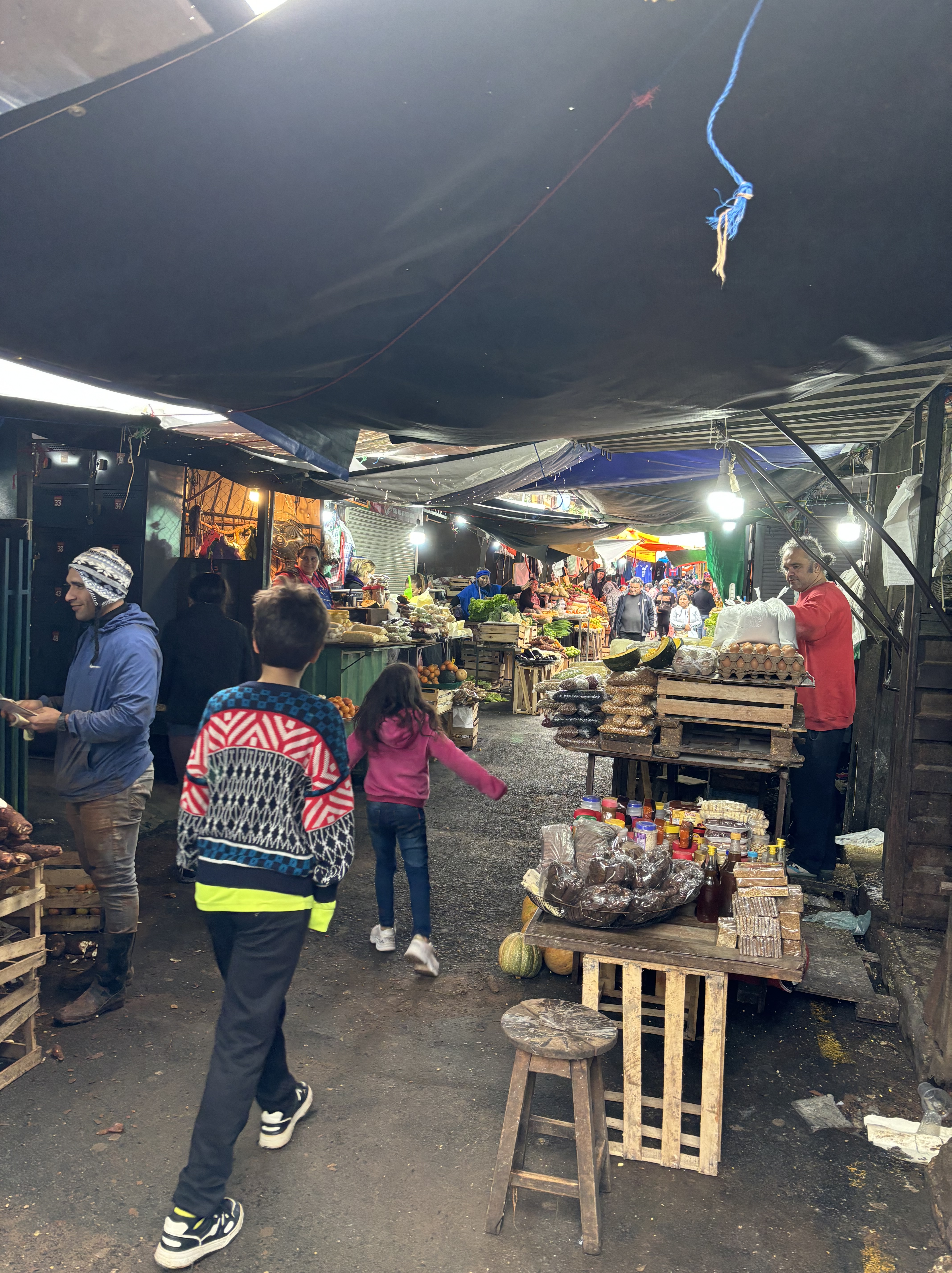 Narrow market alleyway filled with vendors selling a variety of fresh produce.