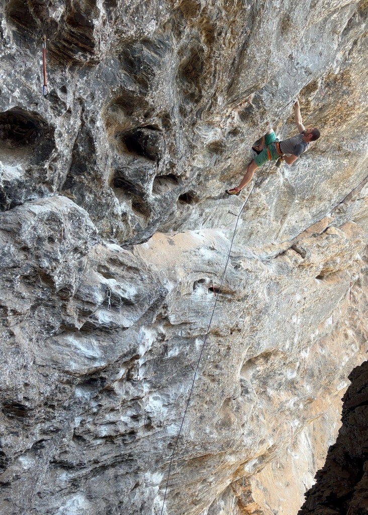 Climber chalking up in a kneebar, ready to make the next move in a steep cave. 