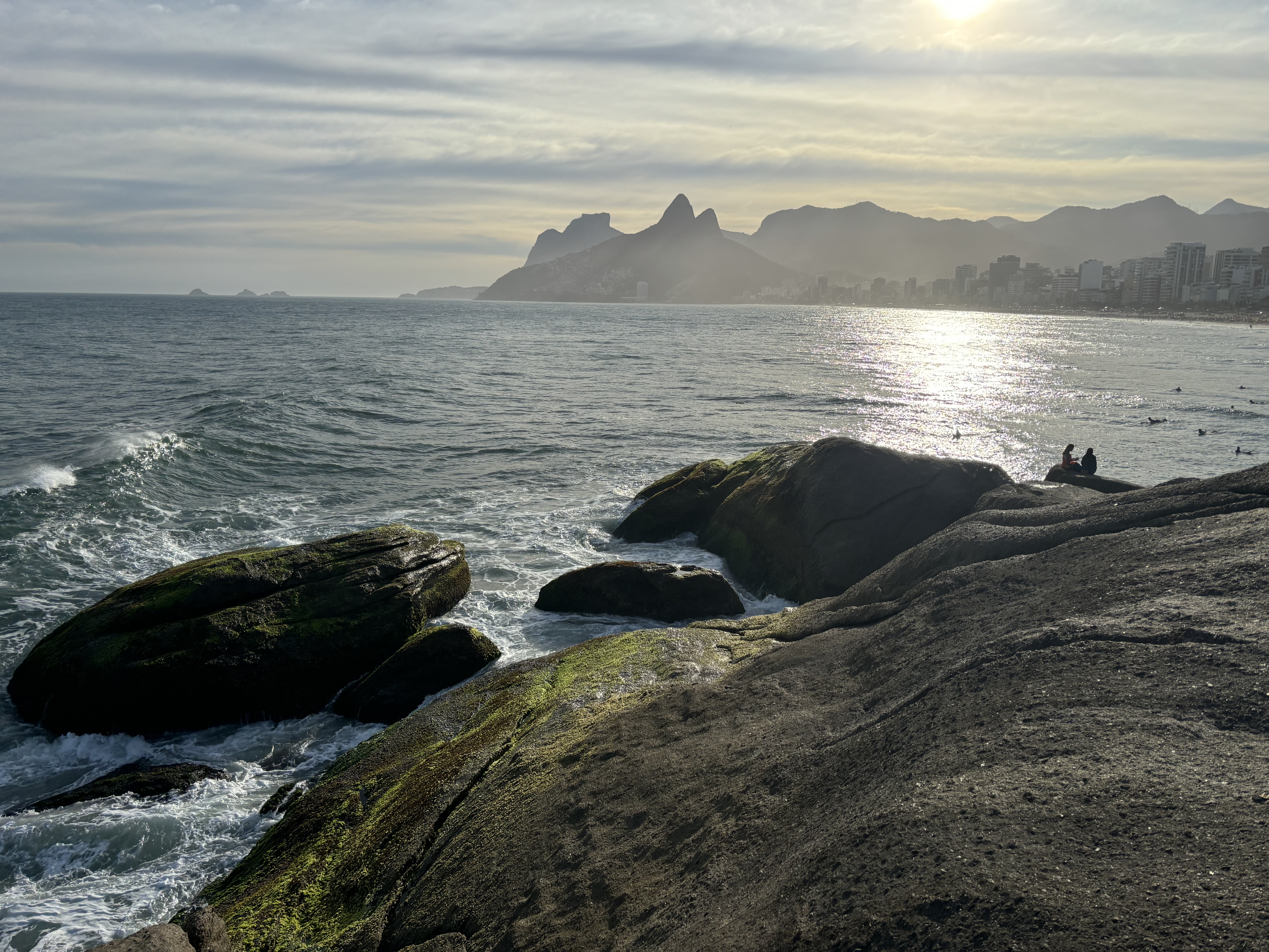 Swimmers enjoying the ocean with dramatic mountain formations in the background, overlooking the city skyline of high rises.