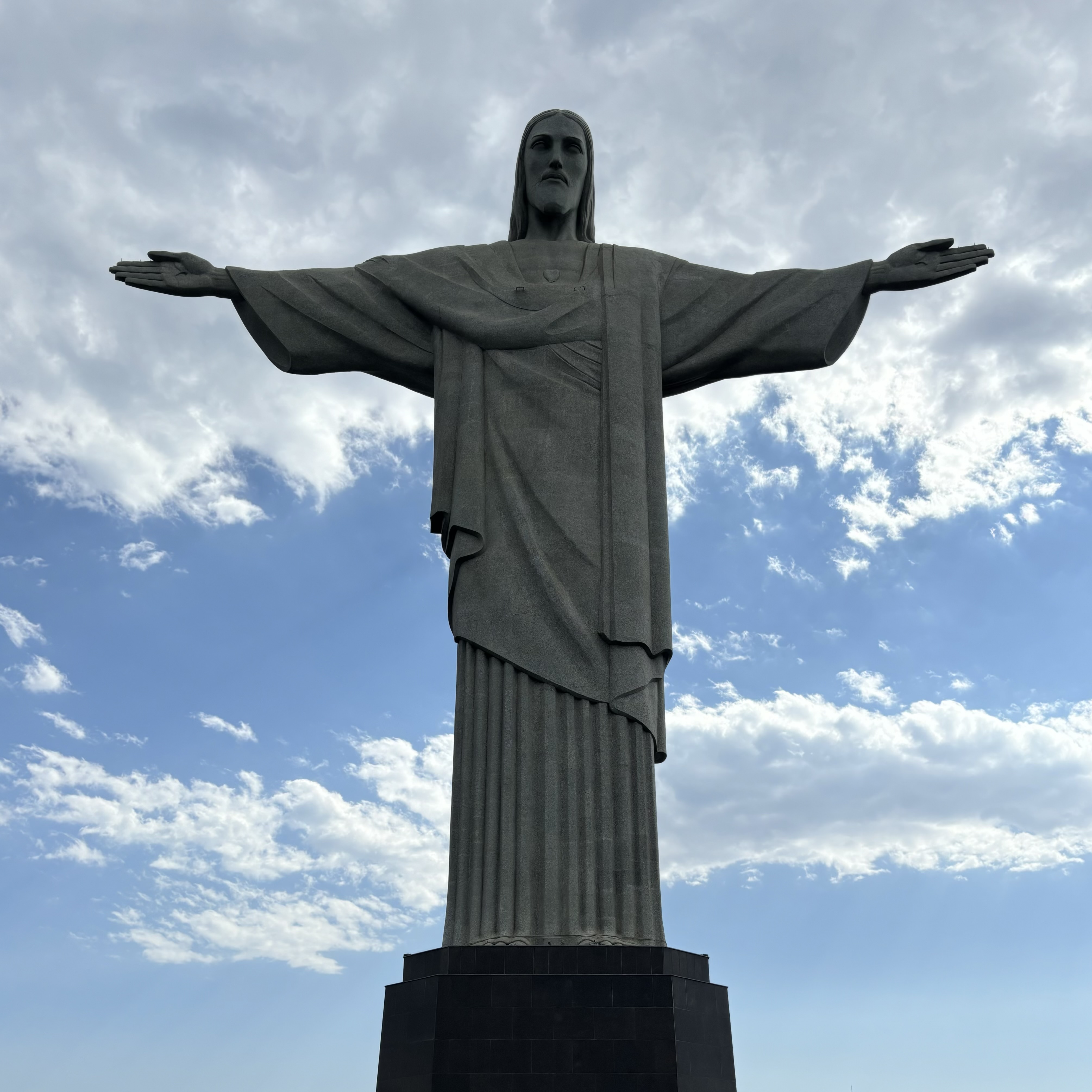 The famous Christ the Redeemer statue standing tall on a black pedestal set against a slightly cloudy blue sky.