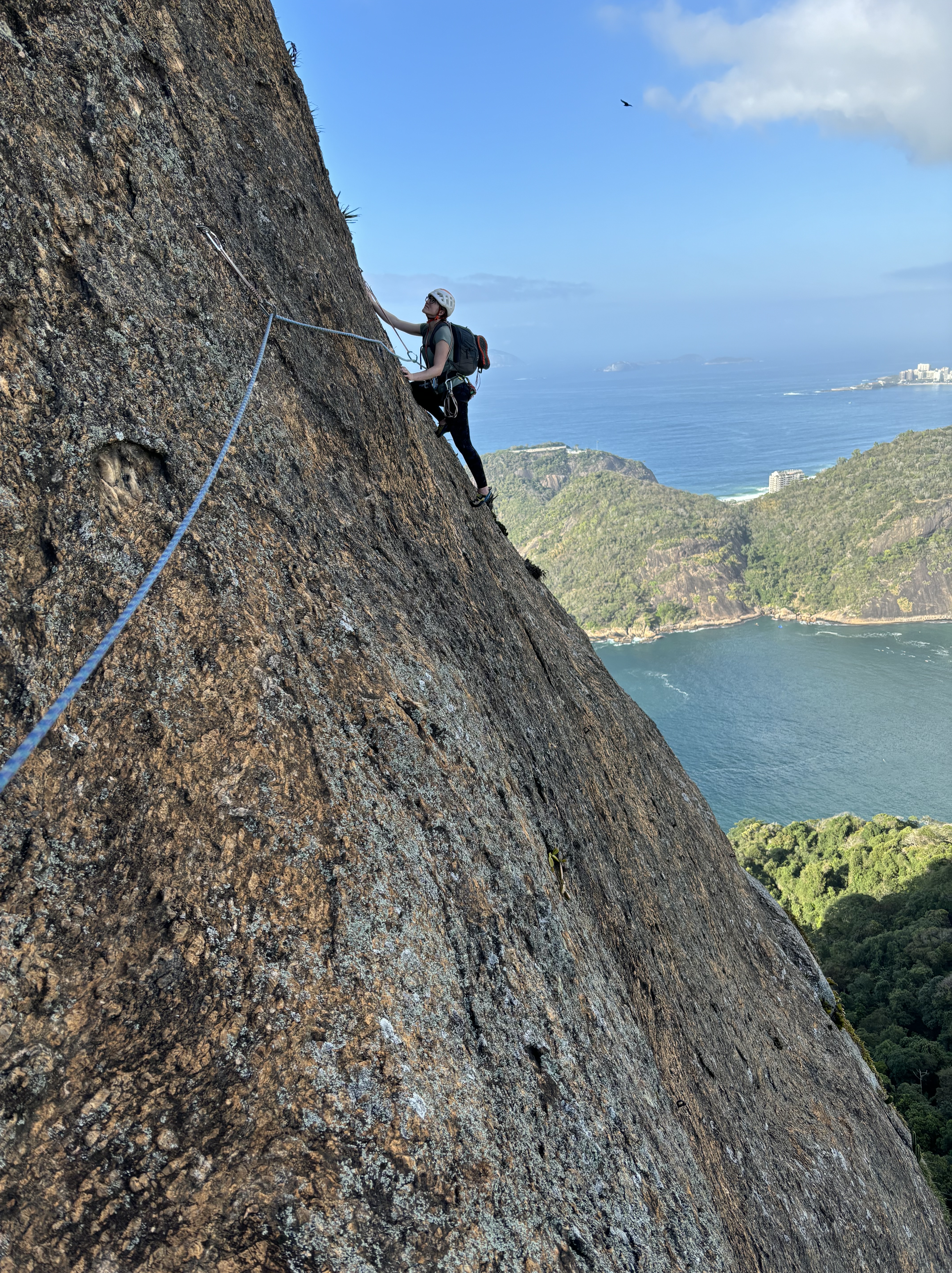 Climber balancing up a slabby face with the bays of Rio de Janeiro's beaches below.