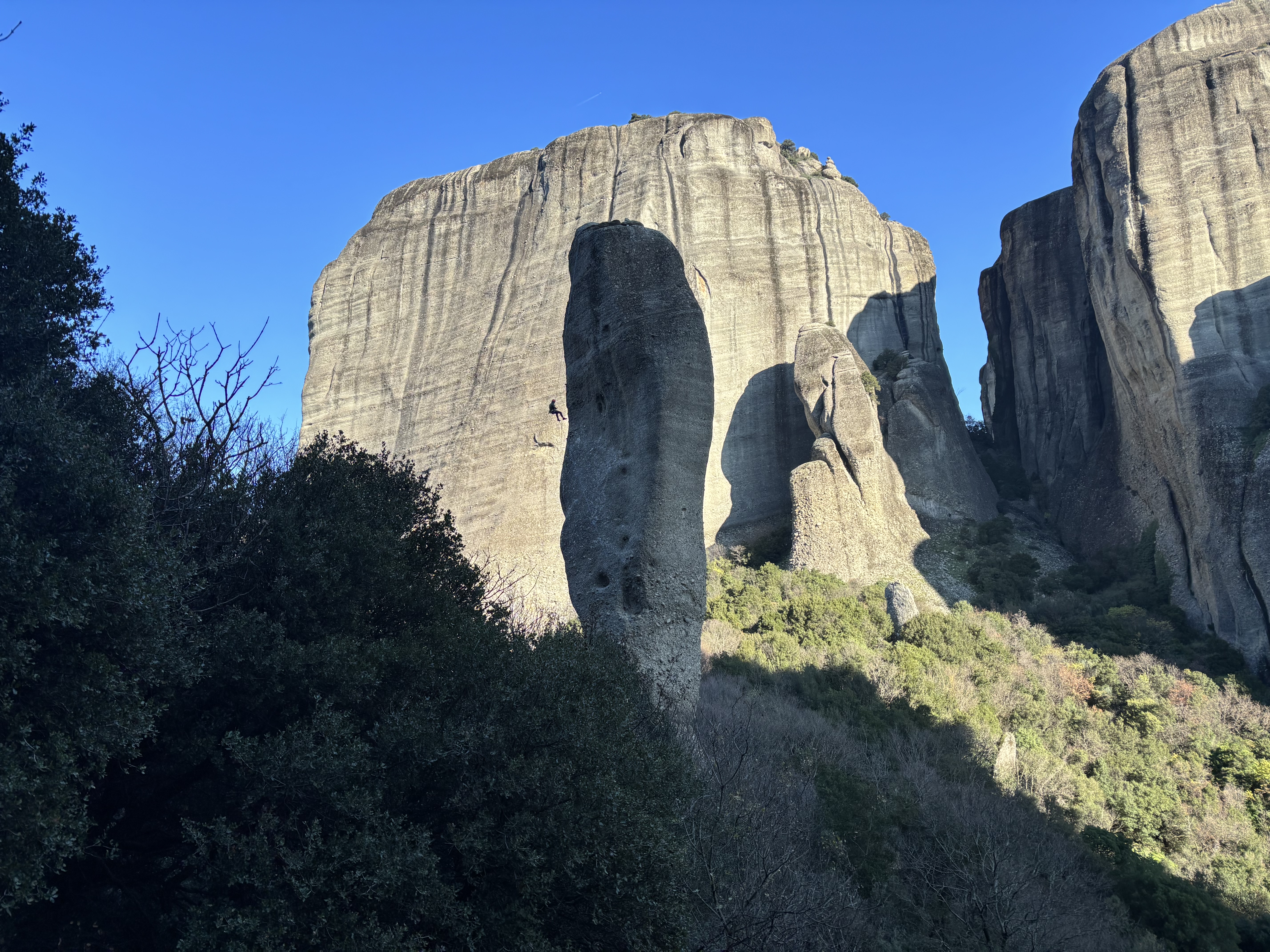 A silhouetted climber abseiling off a tall, thin tower with large buttresses of rock in the background.