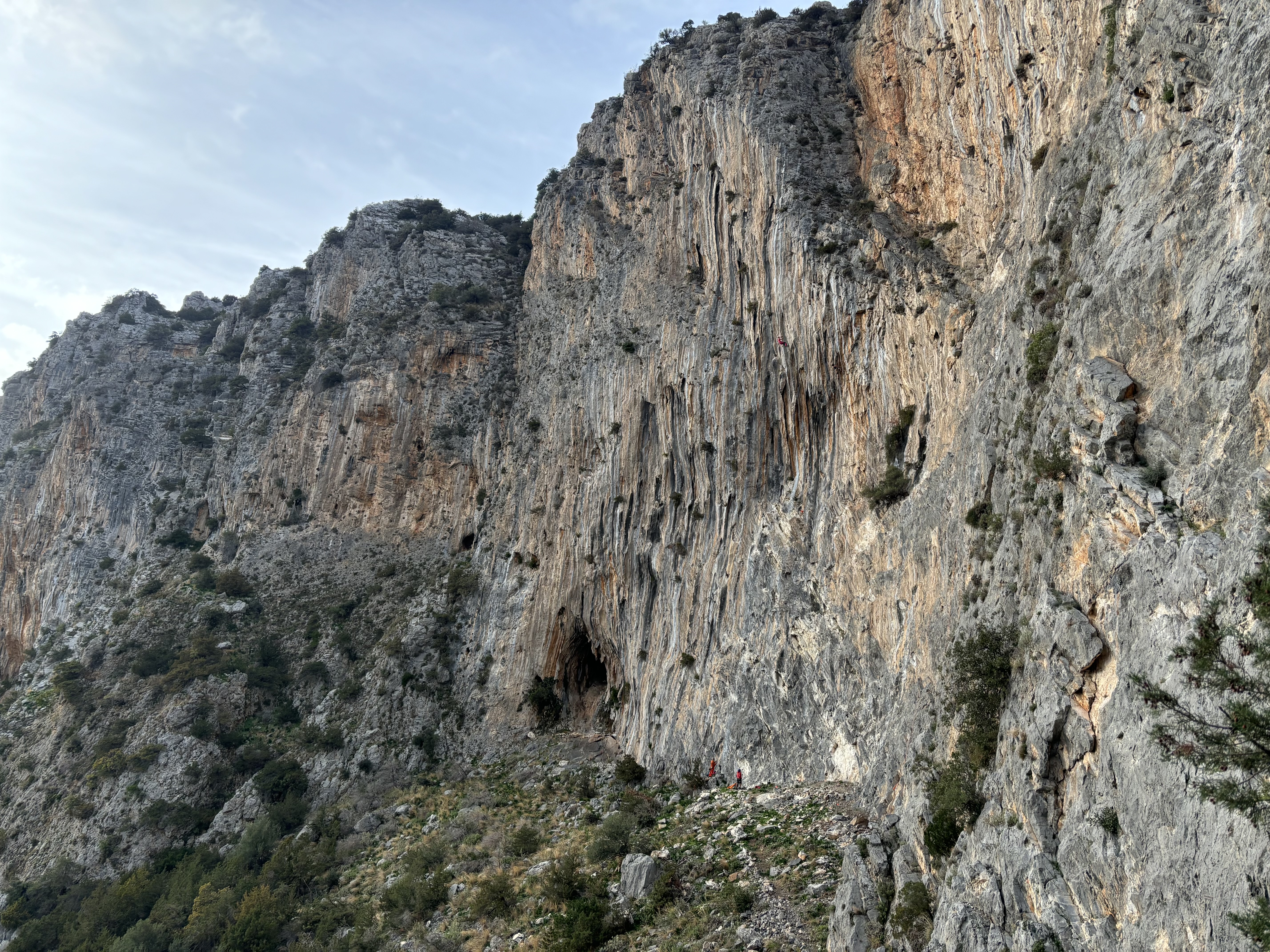 Two climbers dwarfed by huge tufas dripping from the tall limestone cliff.