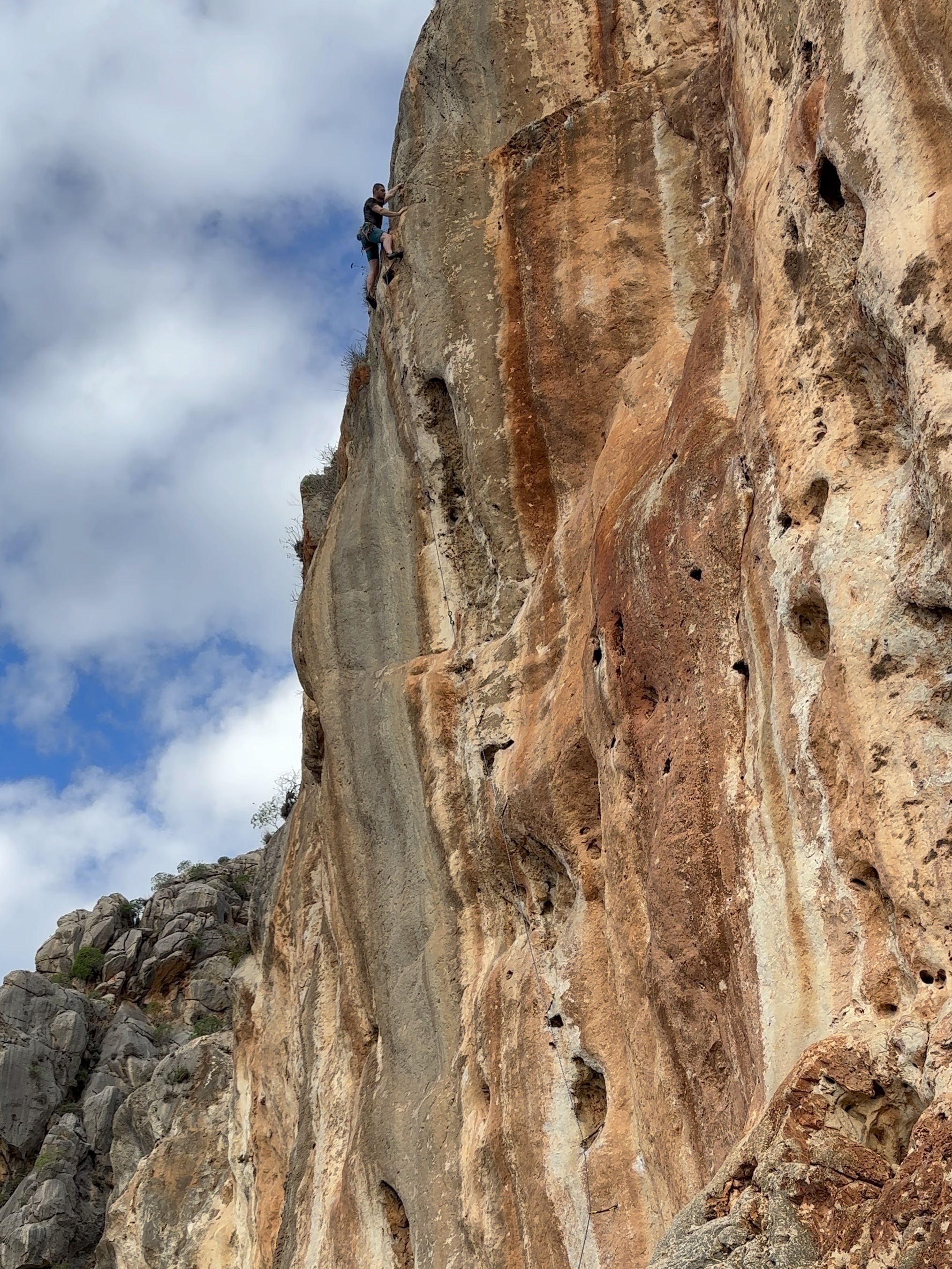 Climber keeping balance high on the arête of a vibrant orange limestone cliff.