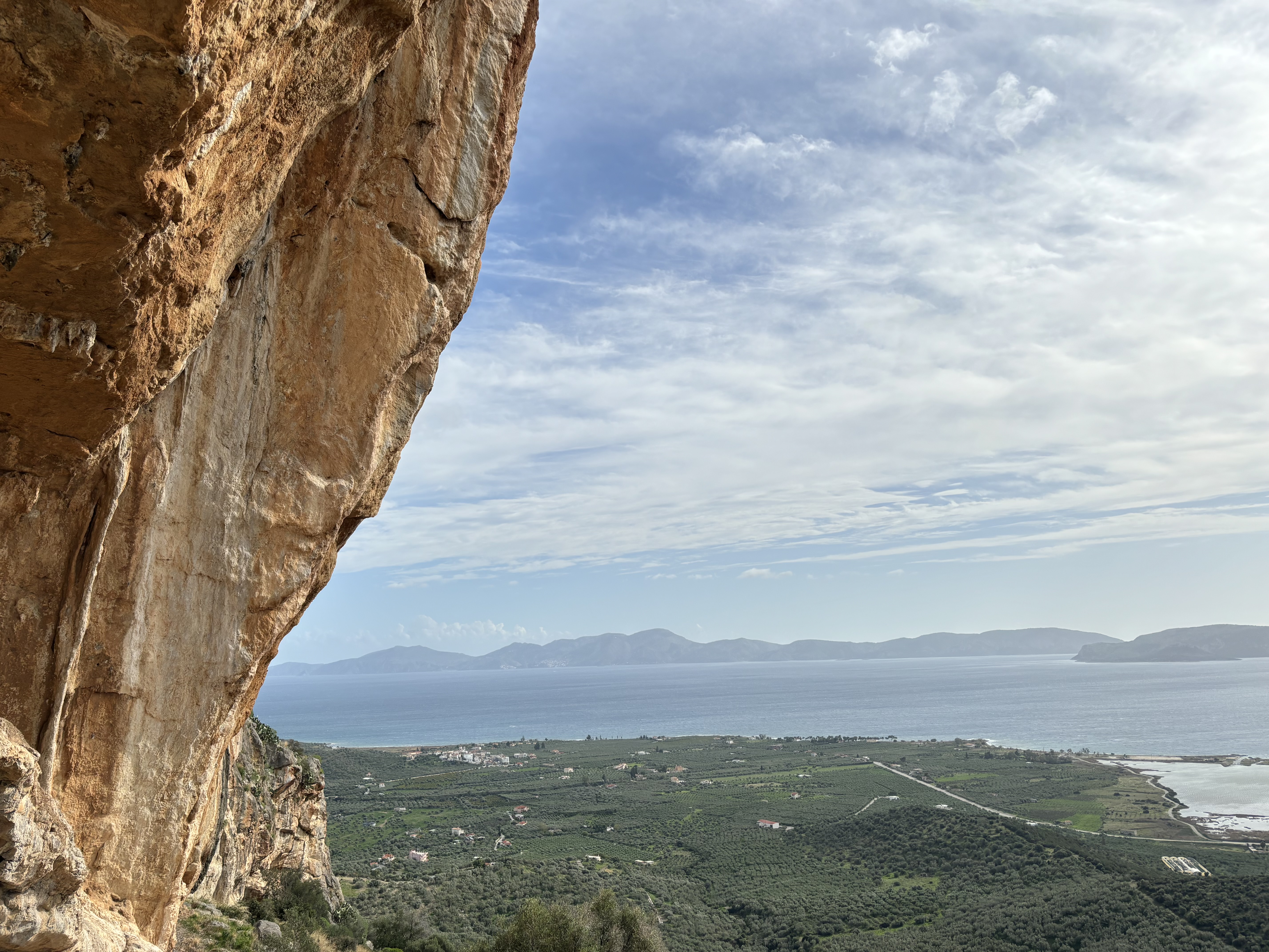 Overhanging orange limestone arête with the sea and mountains in the background.