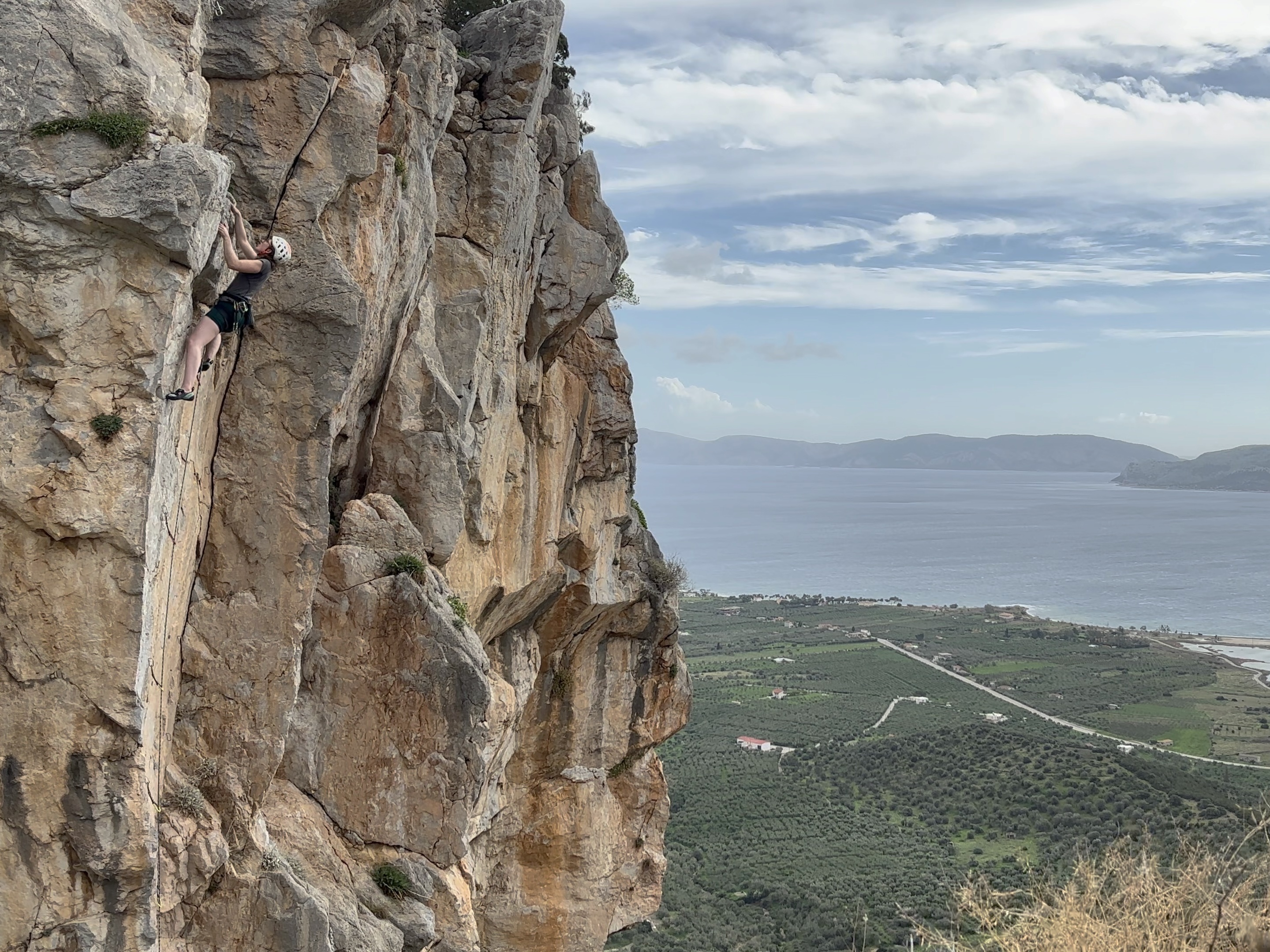 Climber on slightly overhanging limestone wall and arête with the sea in the background.