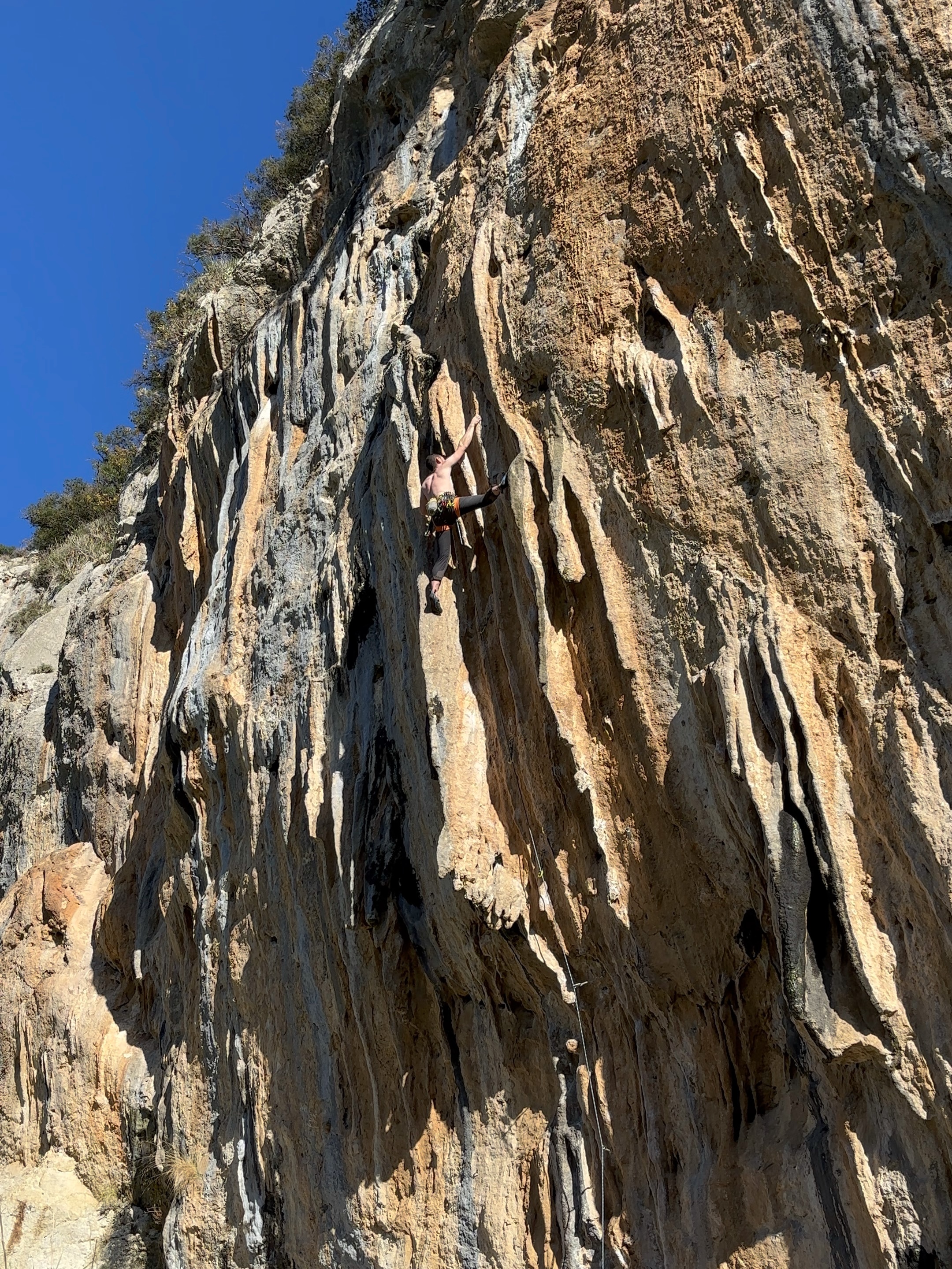 Climber bridging between two large, protruding tufas on an overhanging wall.