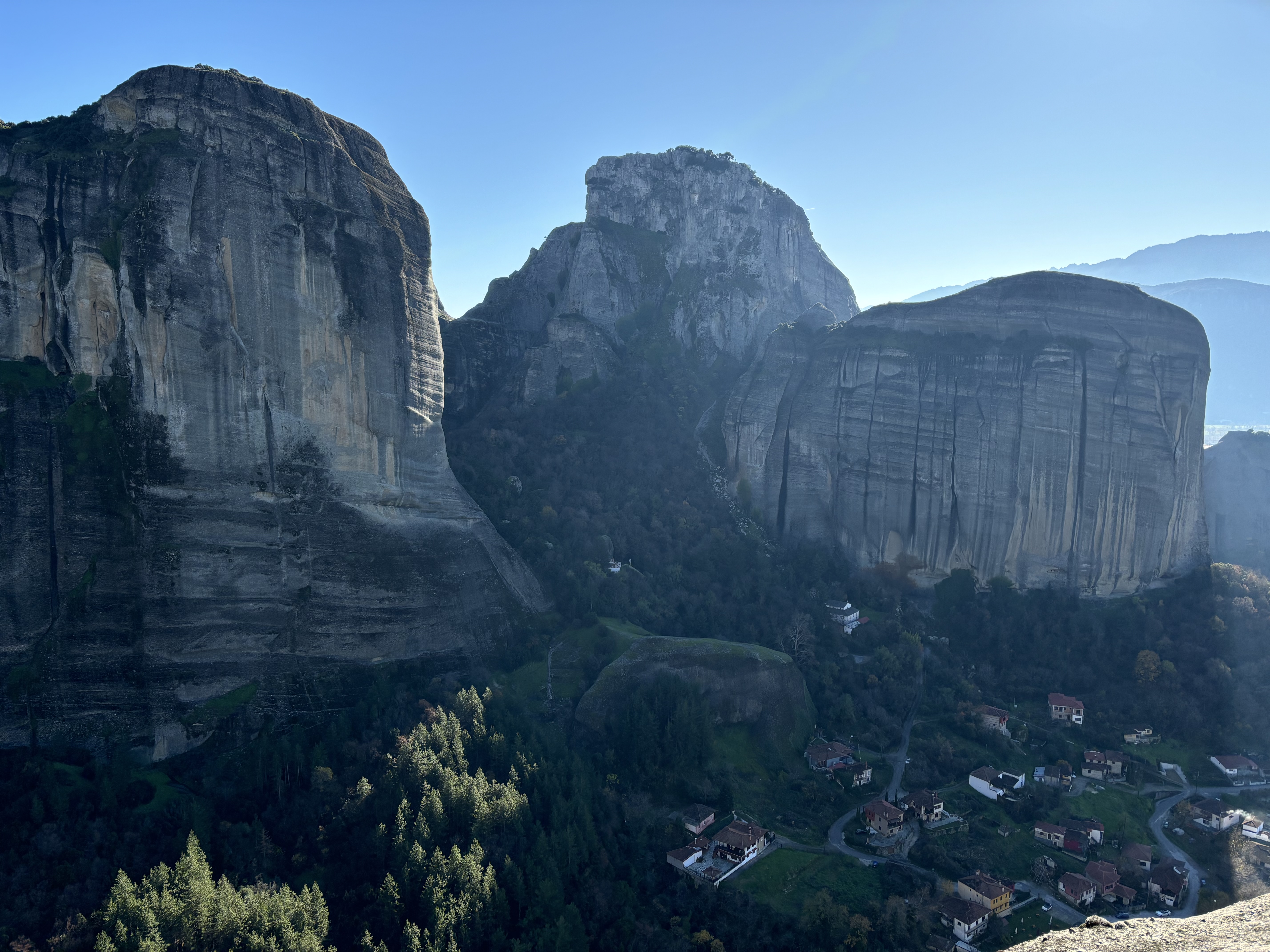 A cluster of houses dwarfed by three large cliffs above, set against a blue sky.