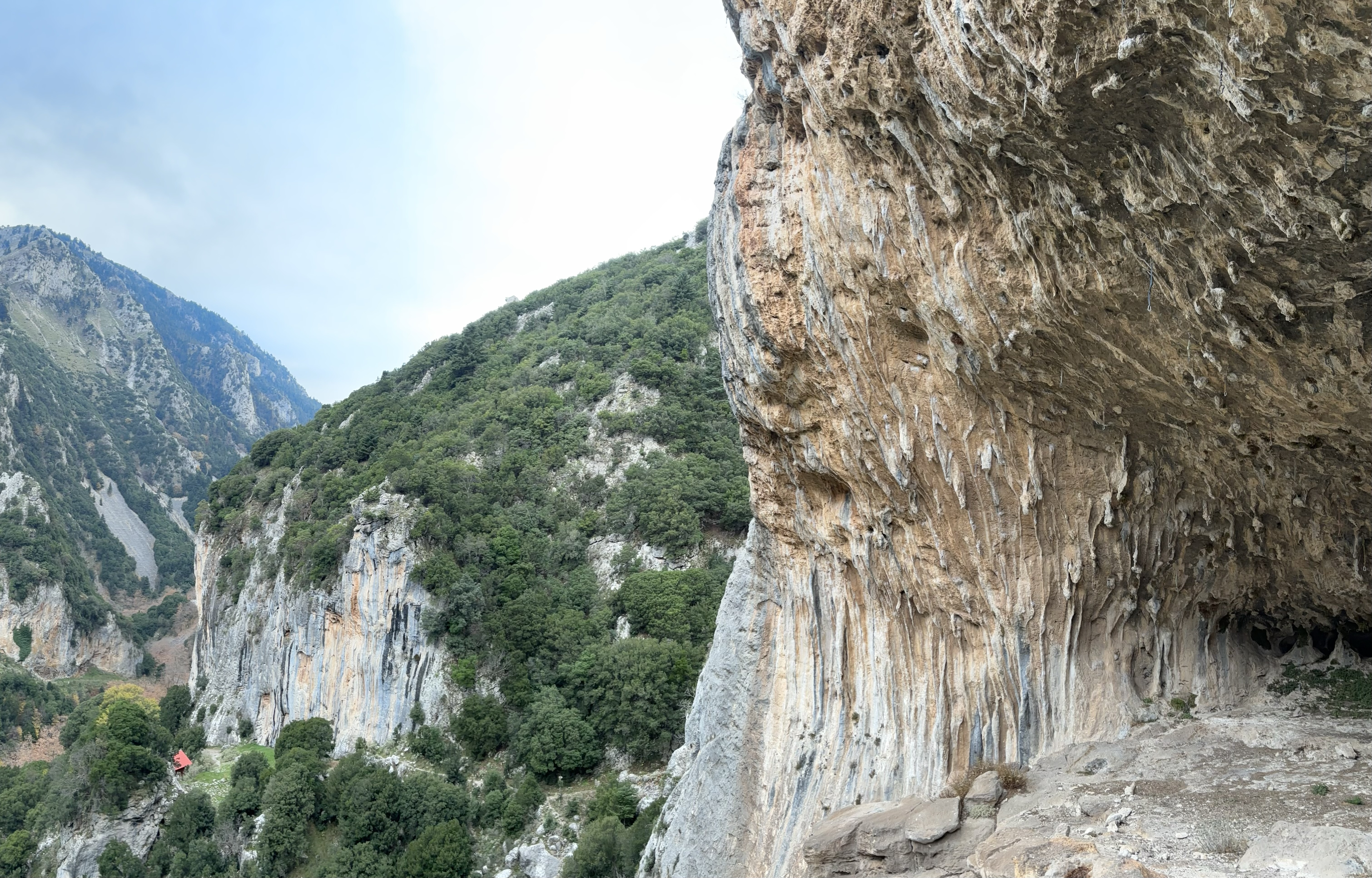 A limestone cave with a steep roof covered in small limestone tufas with an impressive mountainous and craggy valley in the background.