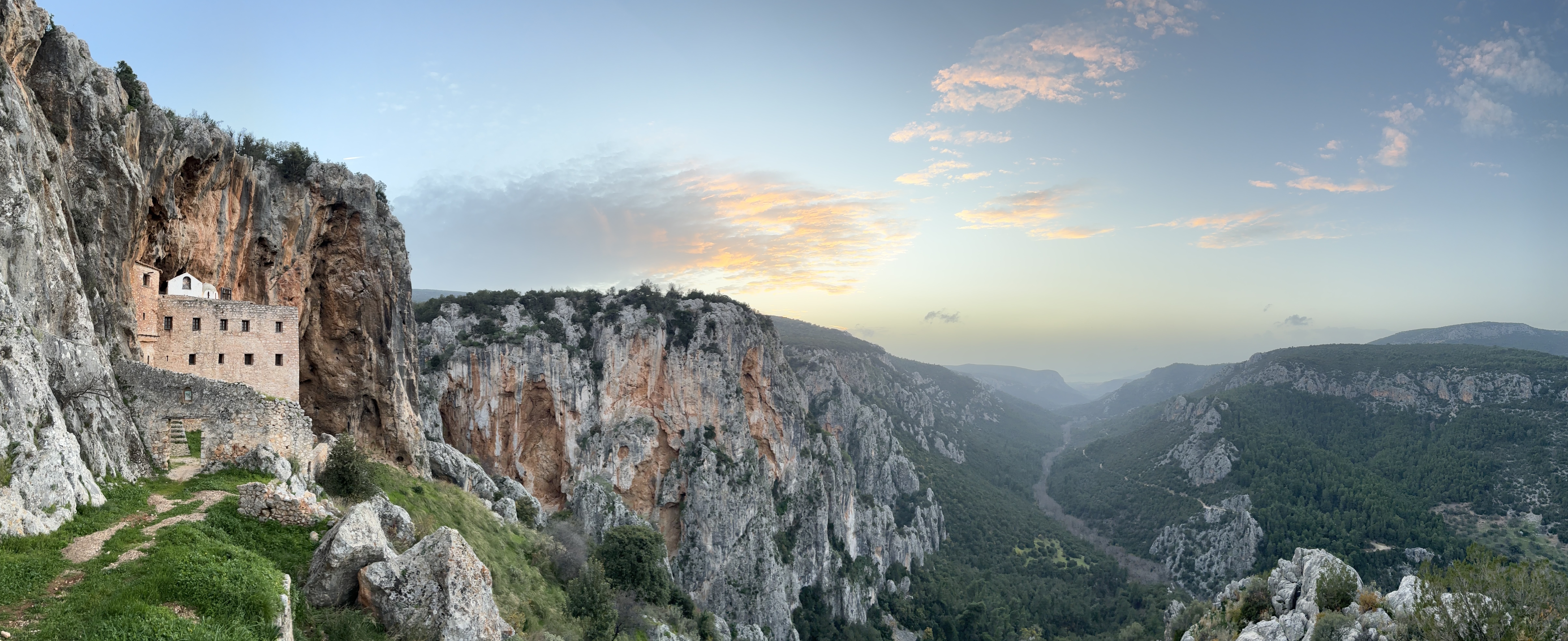 Old, stone monastery built into the cliff high on the side of craggy valley, viewed at sunset.