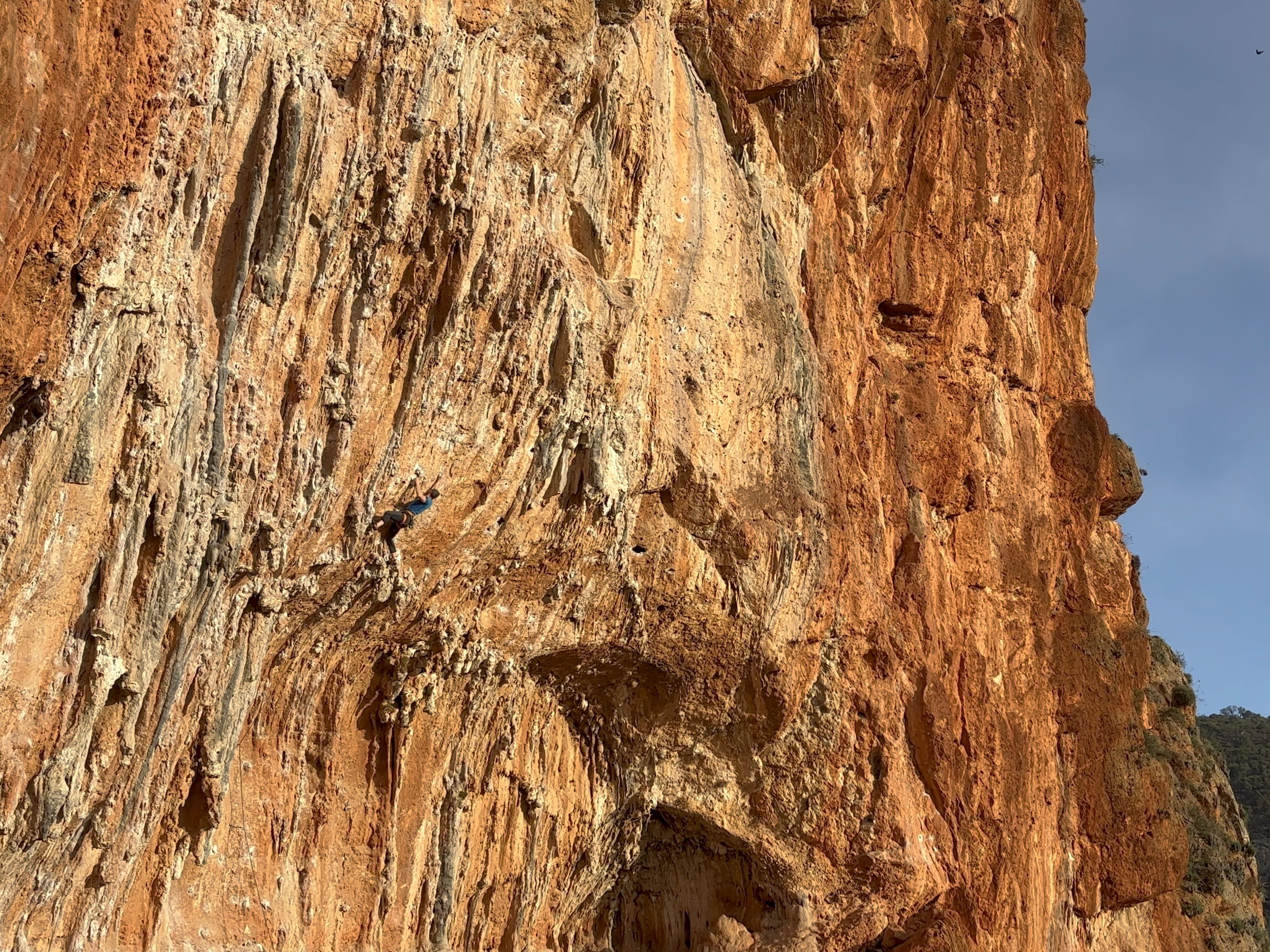 Climber battling a steep, orange limestone wall covered in big tufas and stalactites.