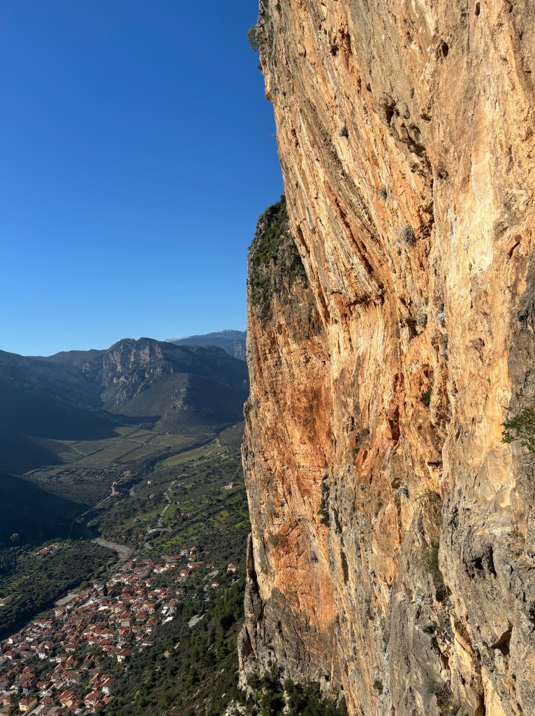 Tall limestone cliff overlooking the terracotta tiled roofs of the village below and the mountainous terrain behind.