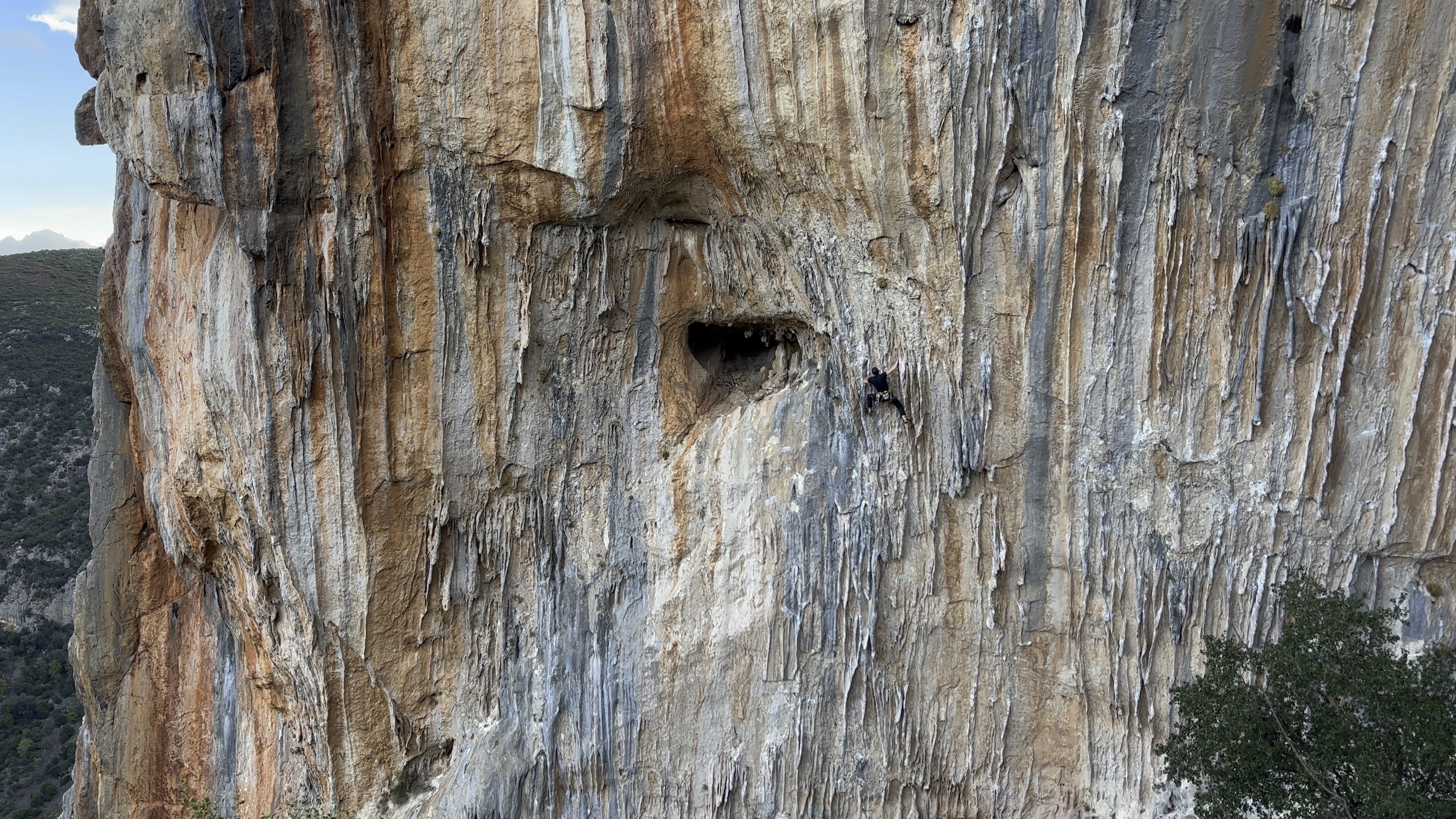 Climber bridging on a wall covered in tufas with orange and blue-grey streaks.