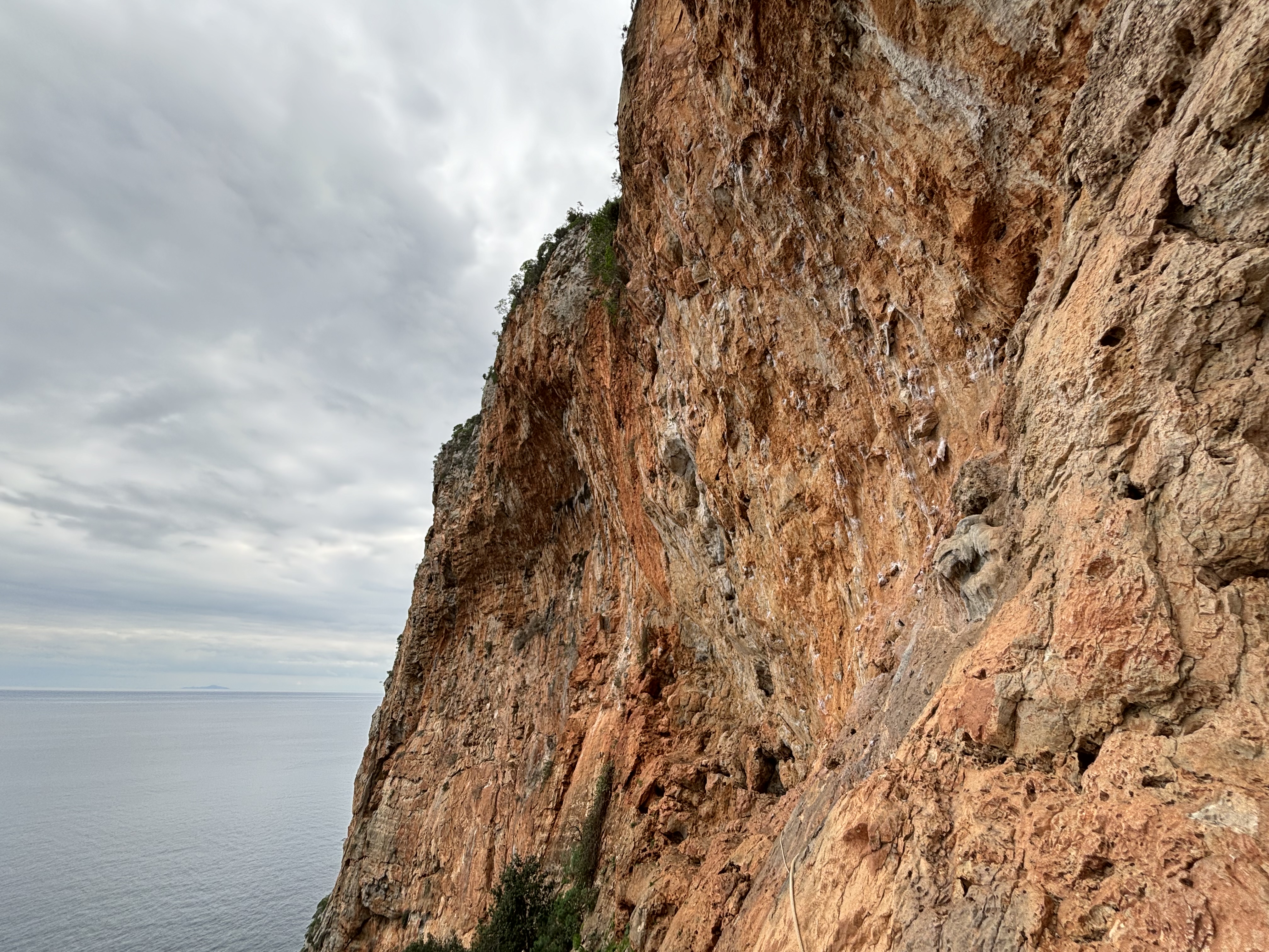 Overhanging orange wall rising from the sea below on a moody weather day.