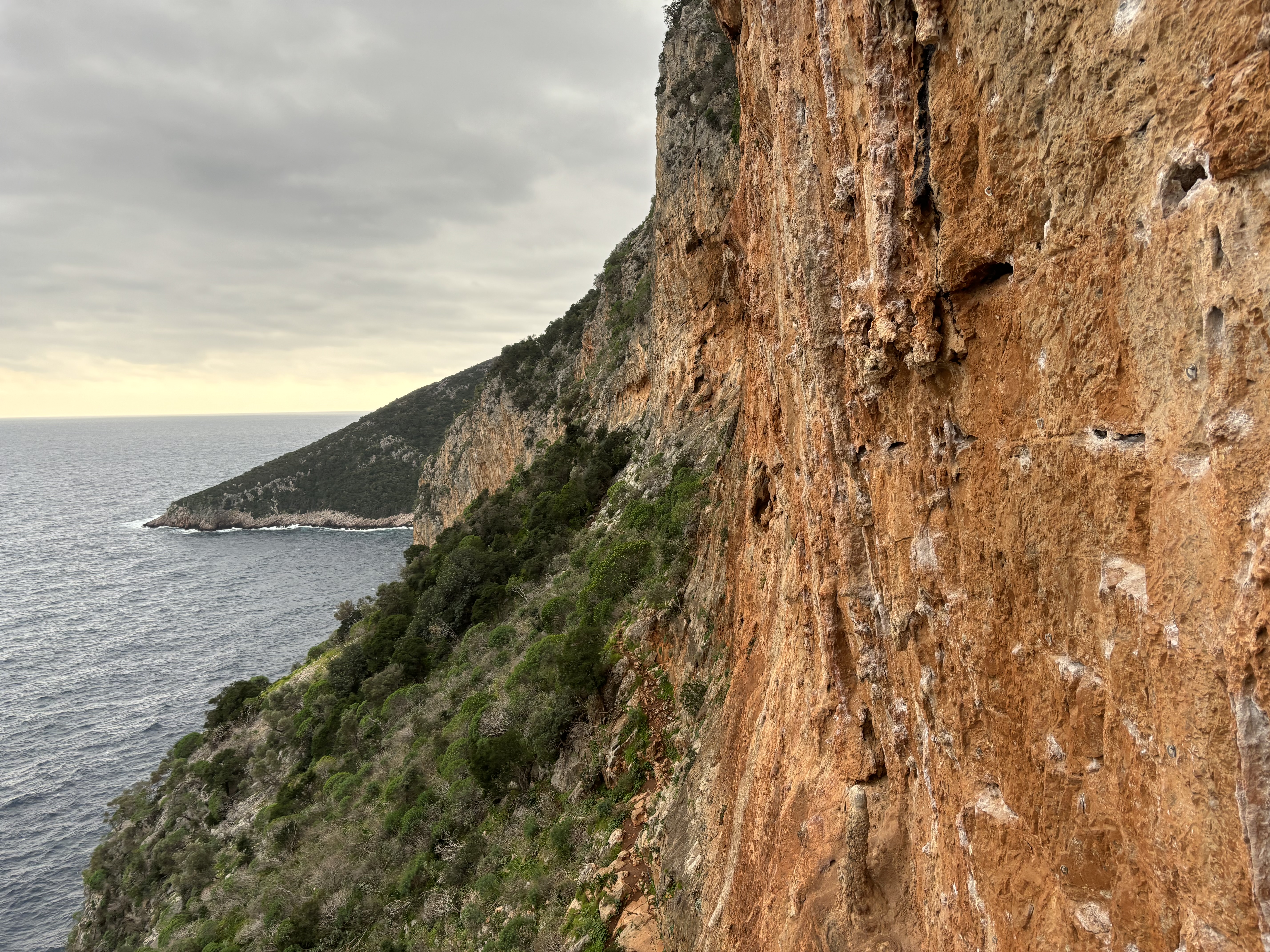 Vibrant orange sea cliff on a balcony above the choppy sea below.