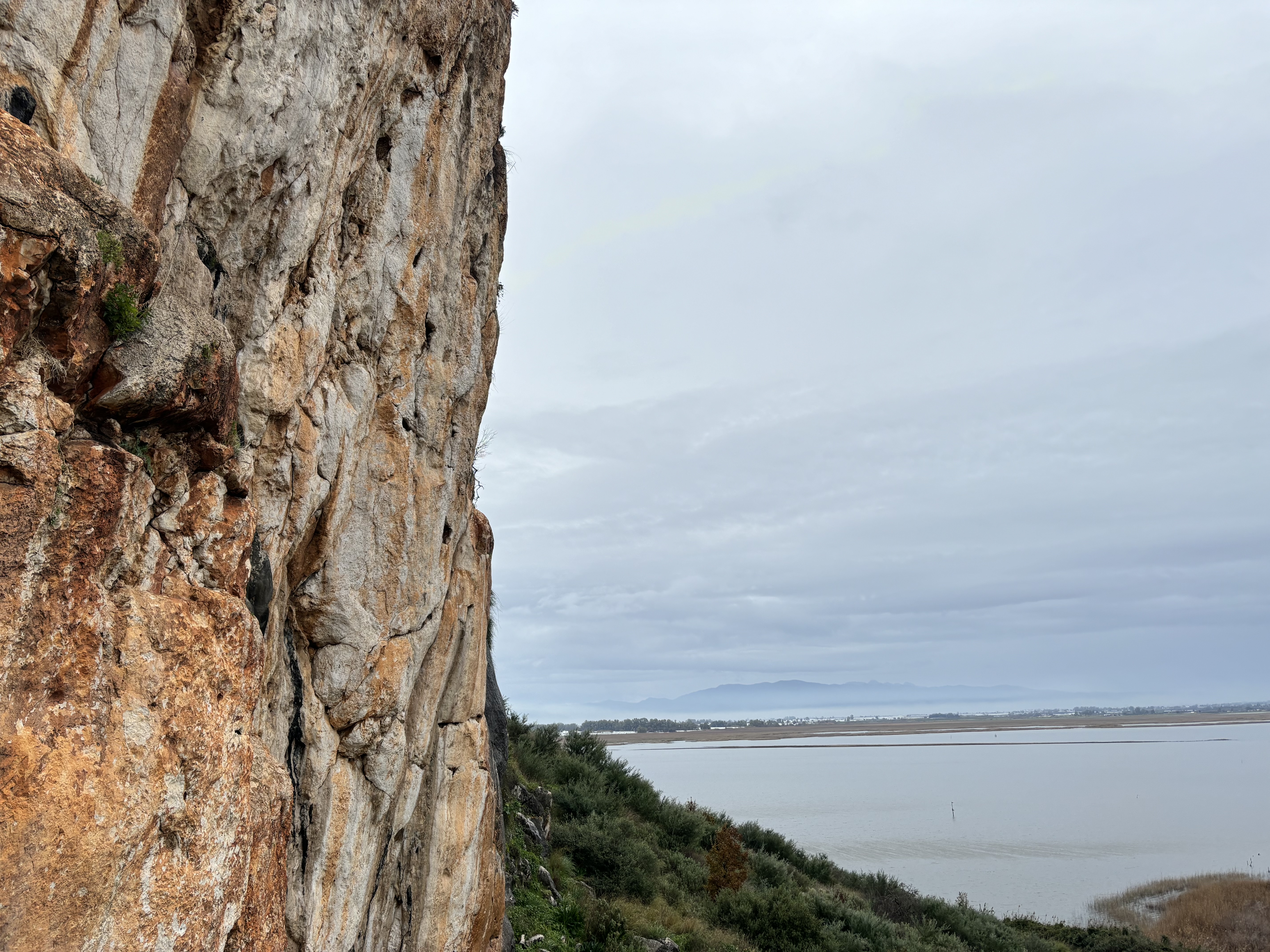 Orange costal limestone cliff overlooking flat marshland with a large mountain silhouetted in the background.