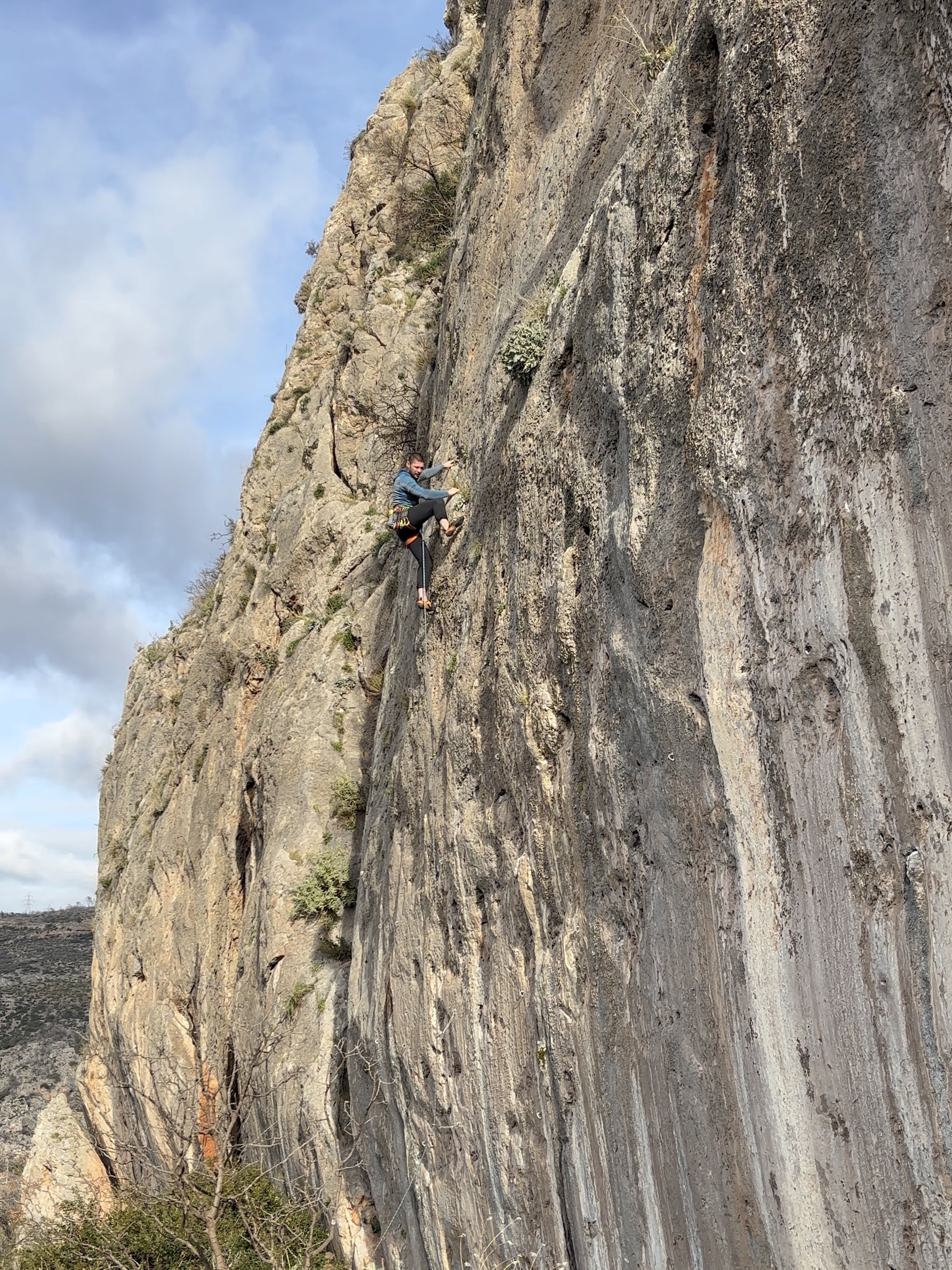 Climber using a high foot on a grey limestone wall with small crimpy features.