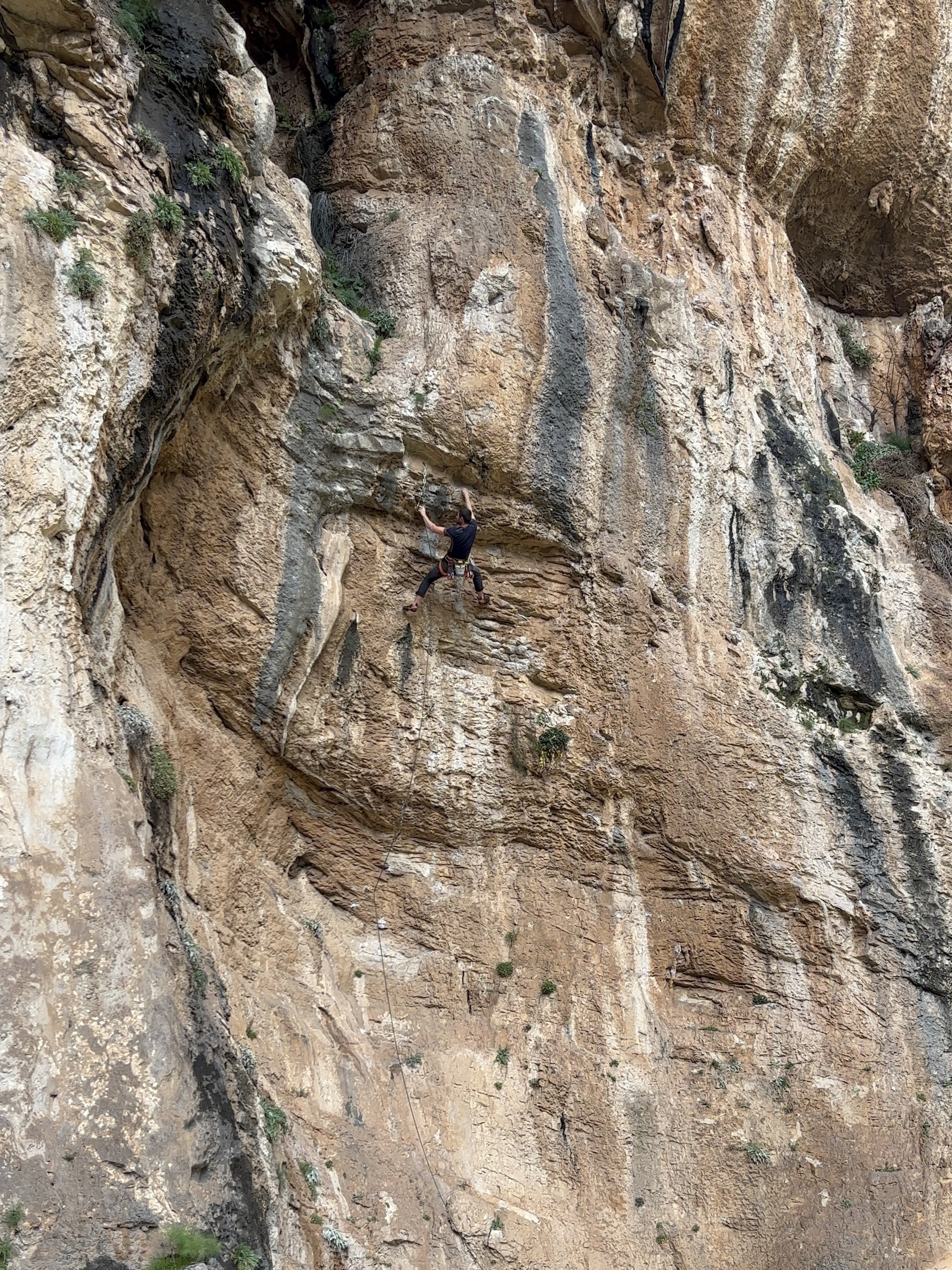 Climber on a steep wall with strata lines that run horizontally along the cliff.