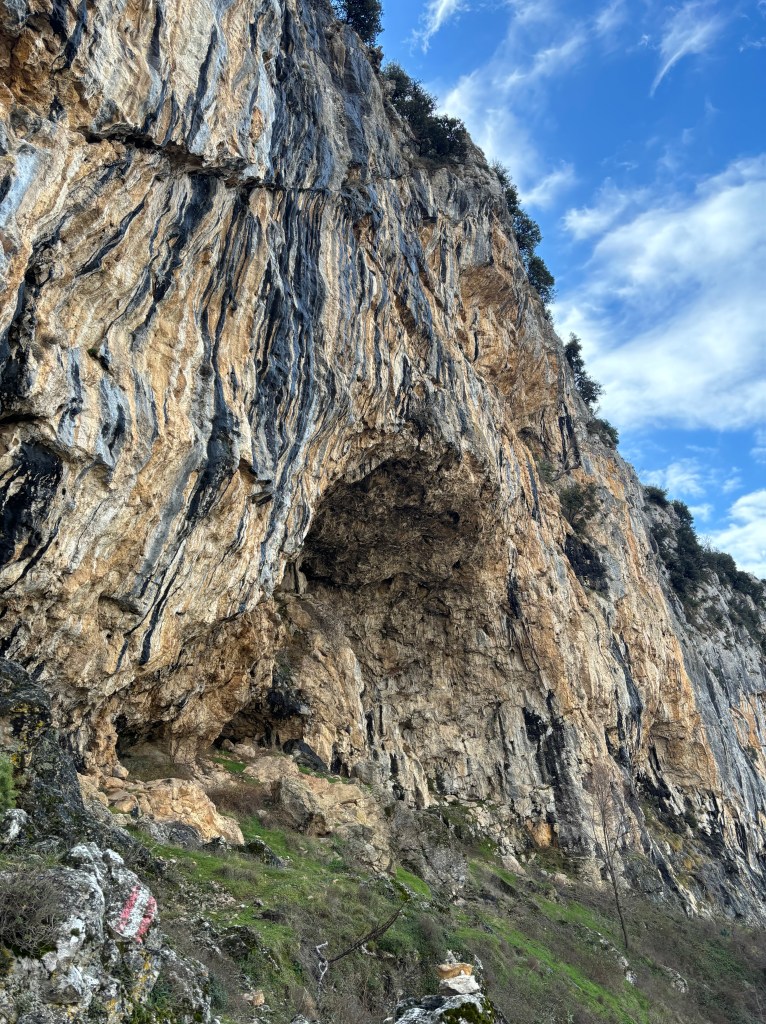 A large limestone cliff face with a circular shaped cave in the middle. 