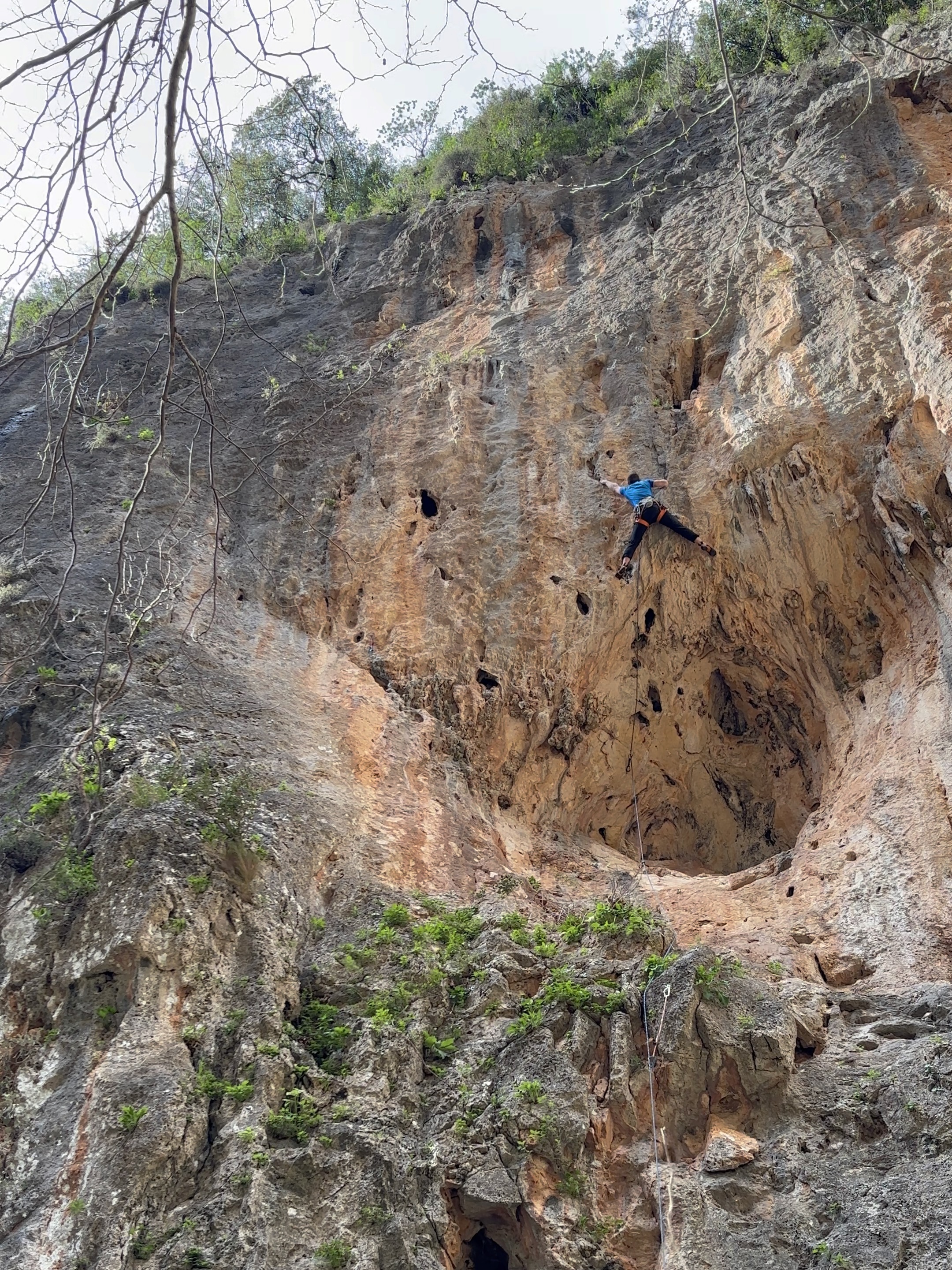 A climber on the apex of an unusual spherical cave feature in the middle of an appealing cliff face. 