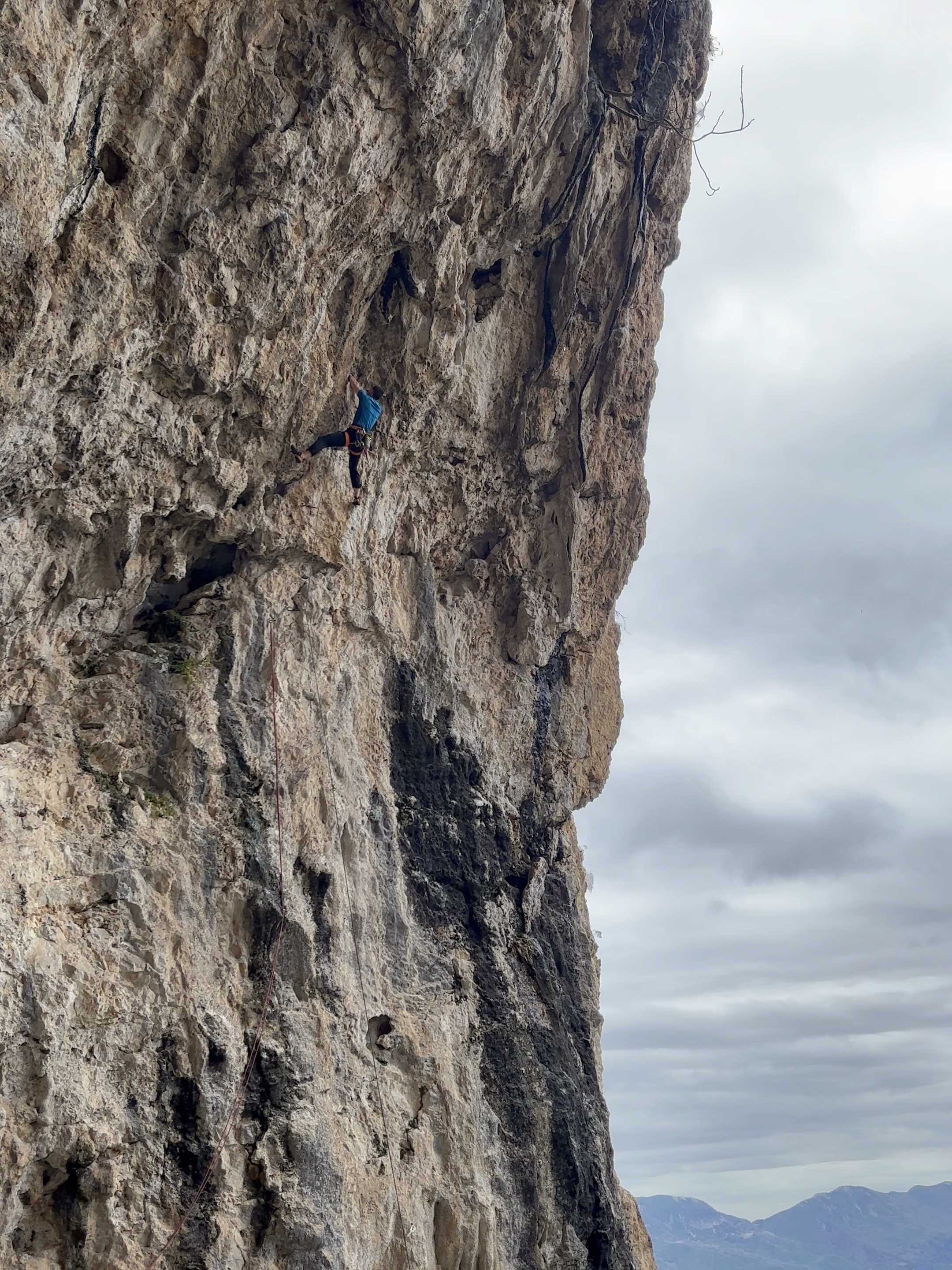 A climber in blue fights the steep overhang of a limestone cave.
