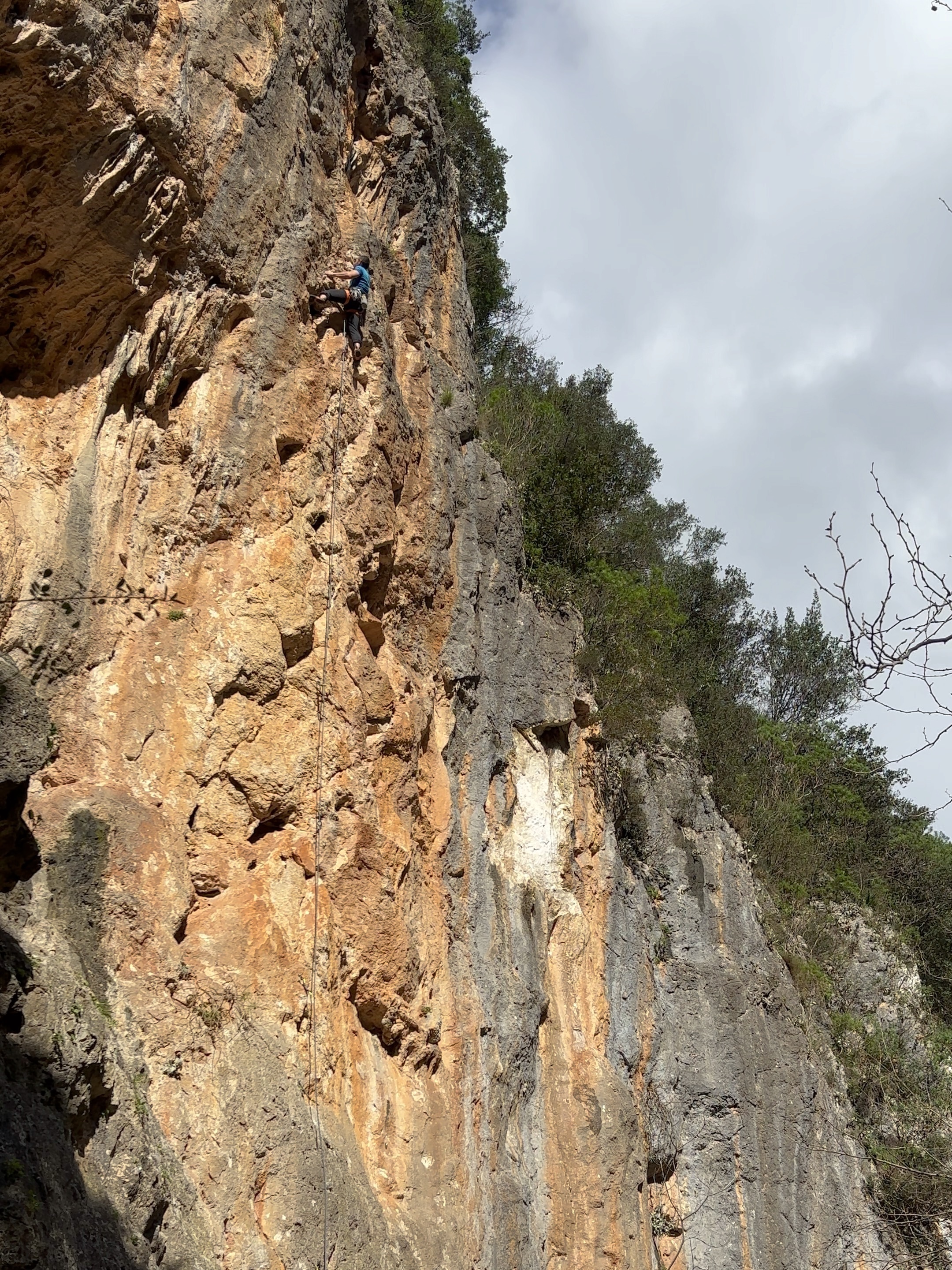 A climber cruises up a long section of orange limestone, with moody atmospheric weather in the backdrop. 