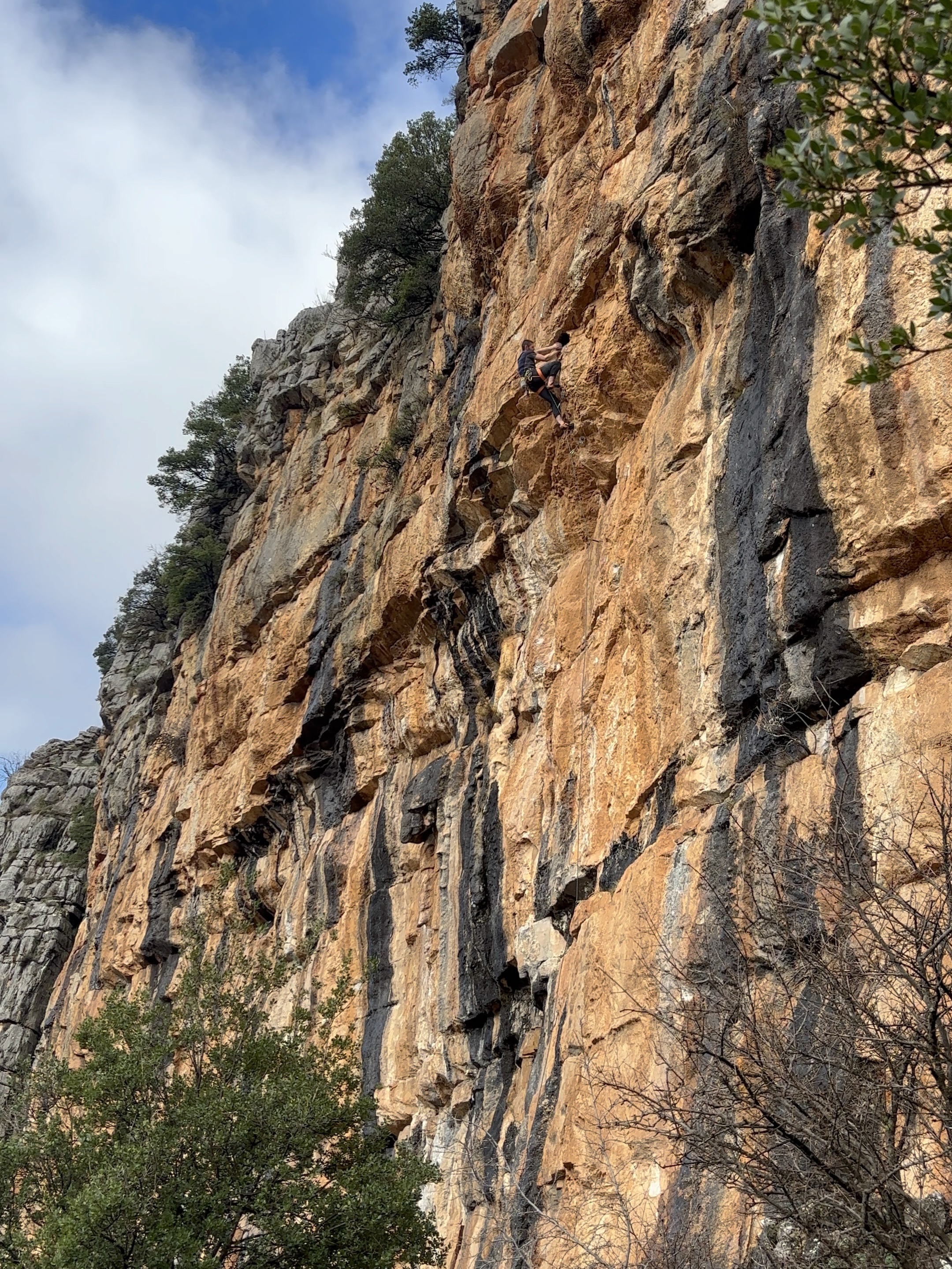 A climber with both hands in a huge jug hold after breaching the steepest part of a roof on a limestone cliff. 