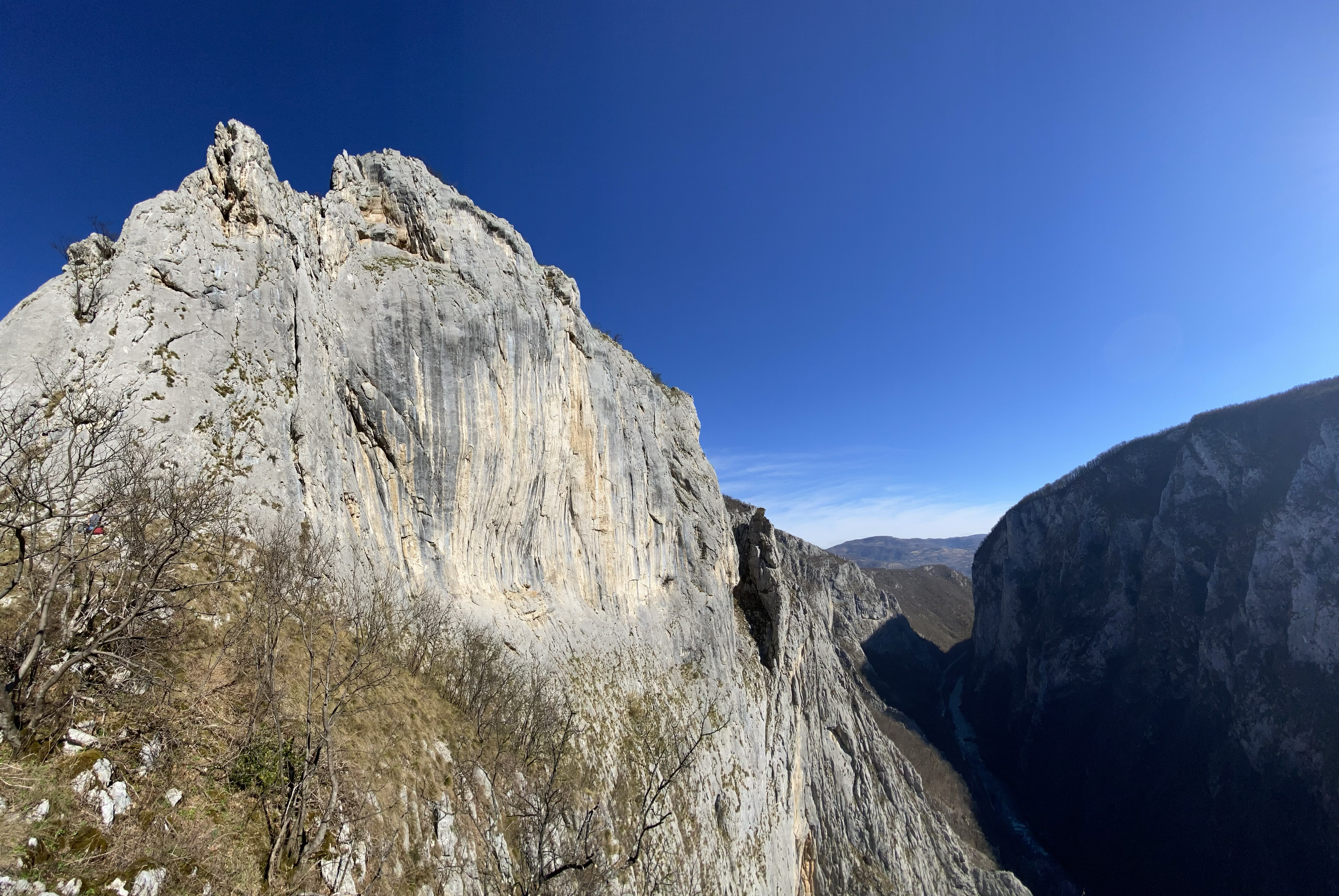 A panoramic view of a huge limestone amphitheatre, that sits proud on top of a deep river canyon with a road through the bottom. 