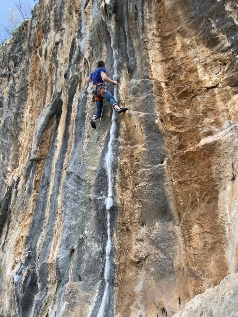A climber battles a single drainpipe tufa on attractive grey and orange striped rock. 